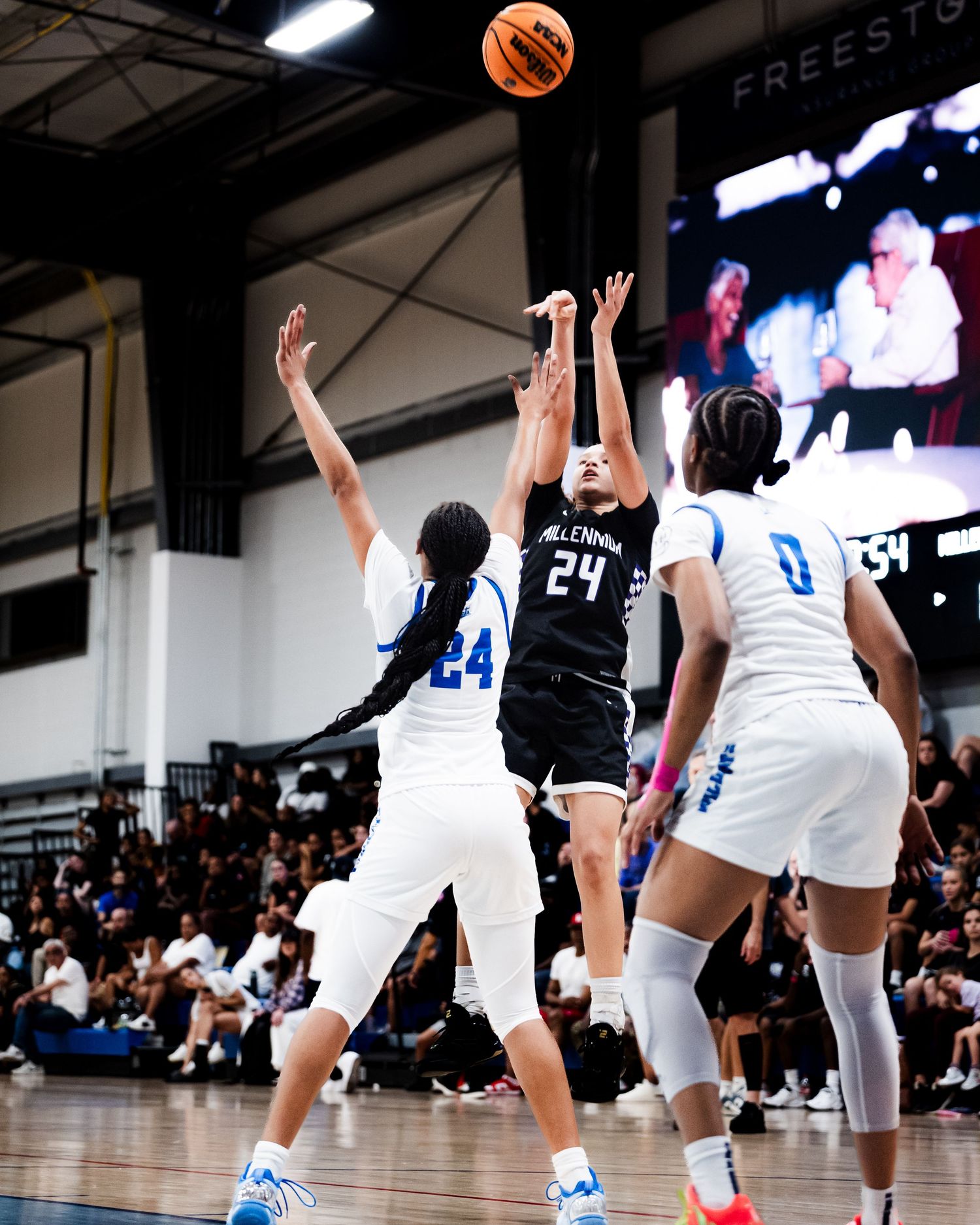 Player #24 in black Millennium jersey shoots over defender during competitive girls high school basketball game.