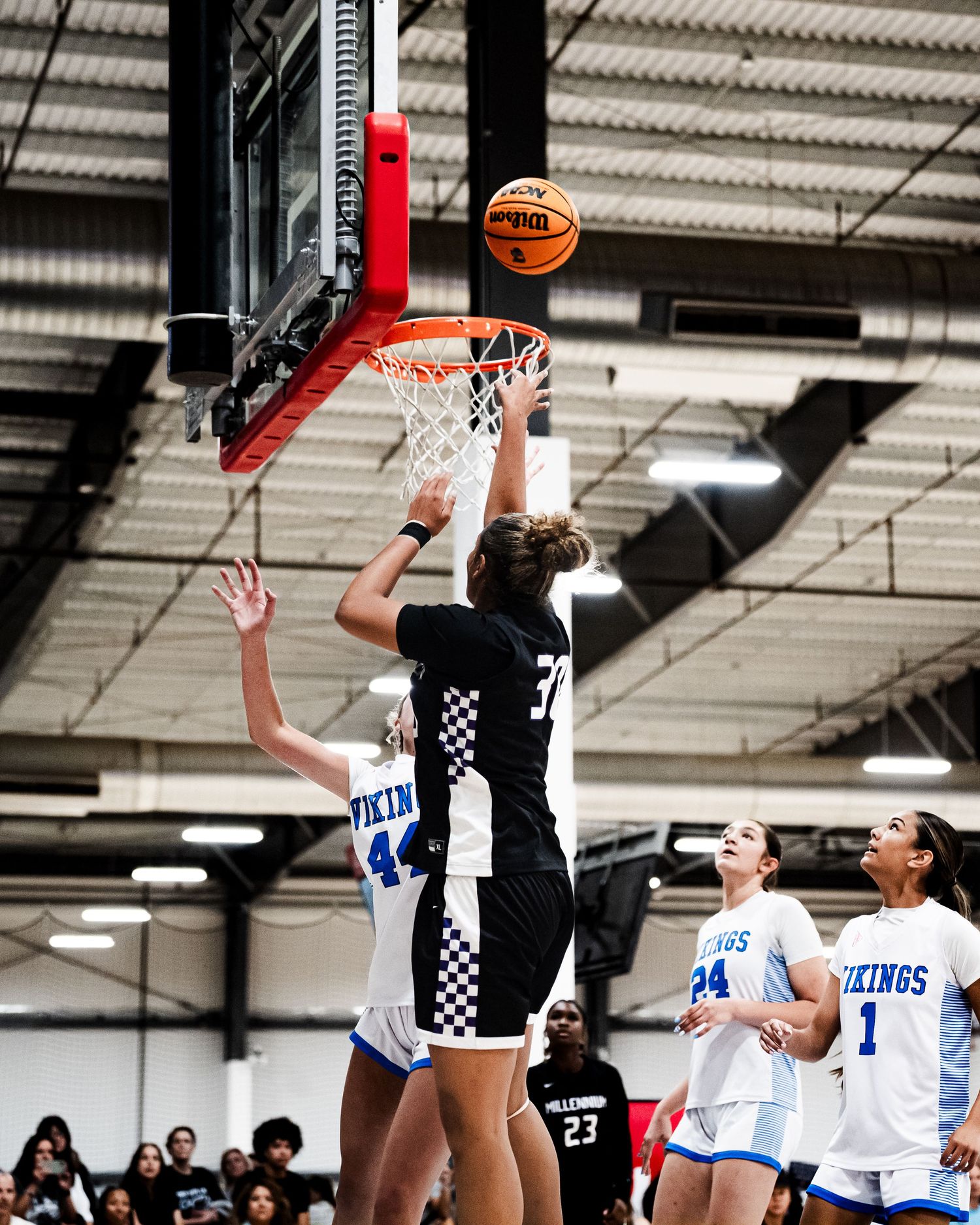 A Knights Basketball player in black dunks over a Vikings defender wearing number 44 during a girls high school basketball game.