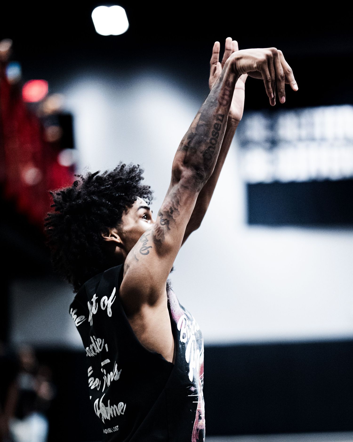 Basketball player in black jersey reaching up to shoot on indoor court.