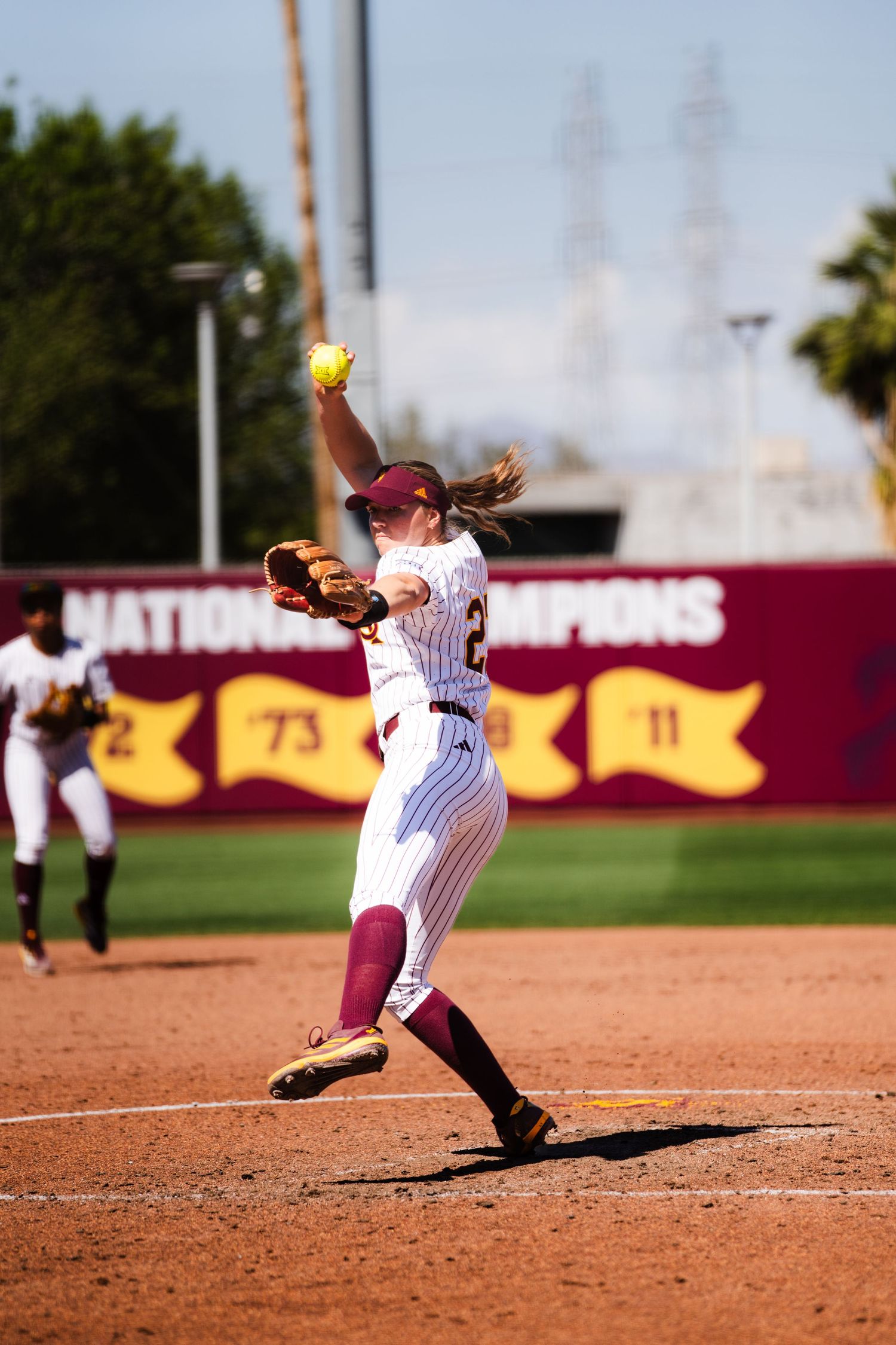 ASU Sun Devils softball pitcher winding up to throw yellow ball during game.