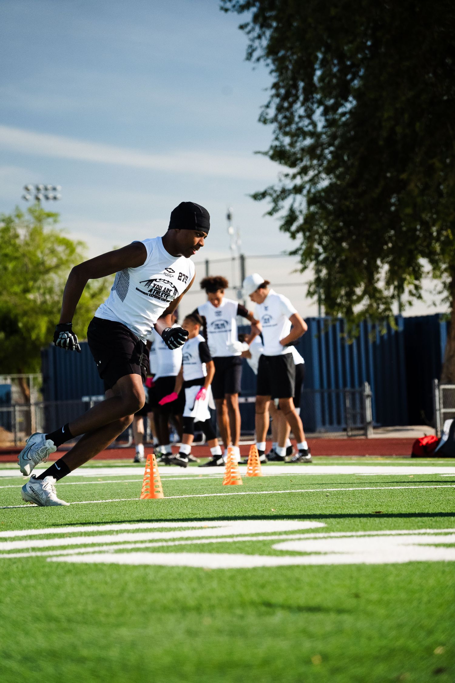 Young athlete in white shirt sprinting through cone drills on green turf field.