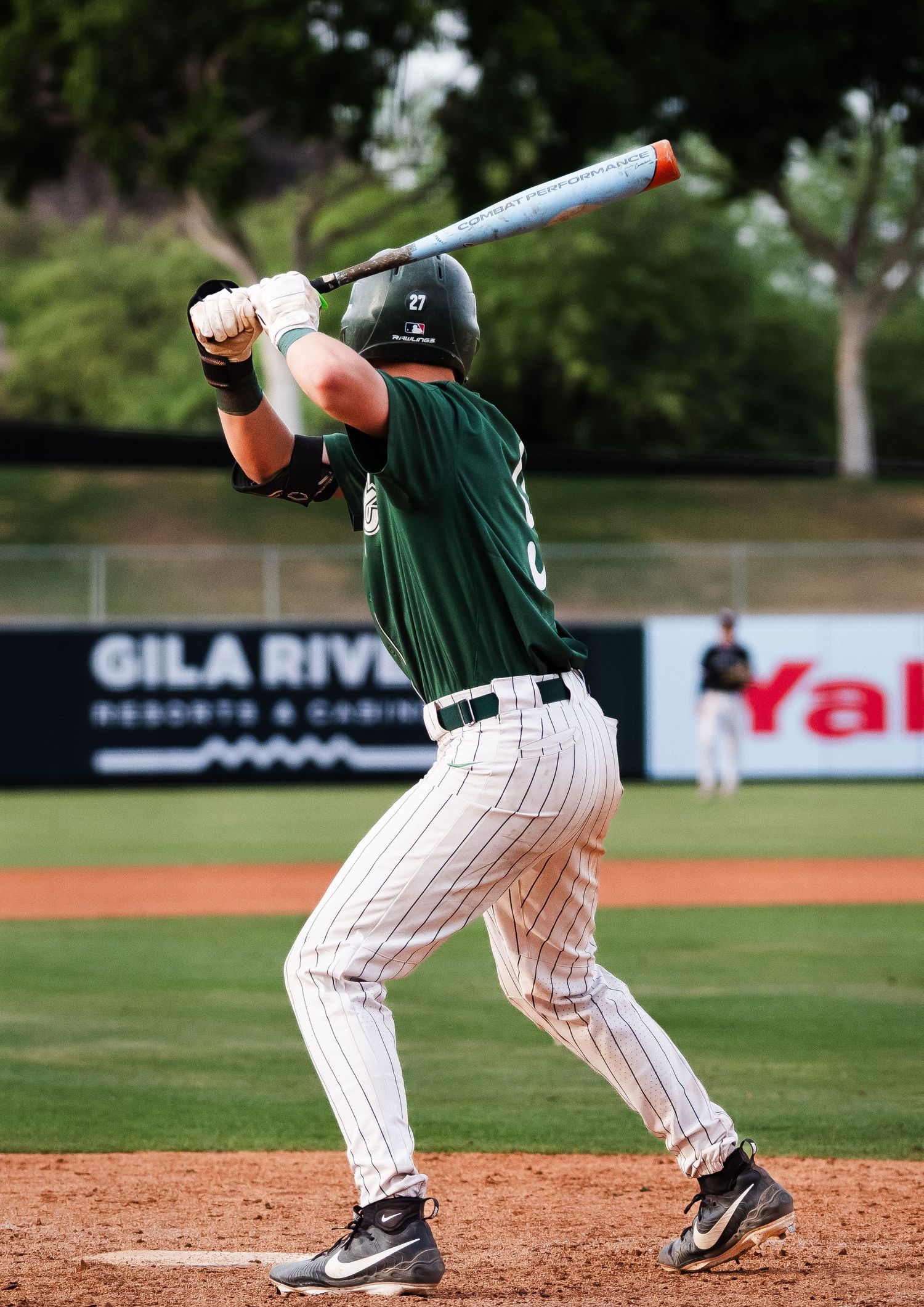 Baseball batter in green pinstripe uniform swinging at pitch at Gila River stadium.