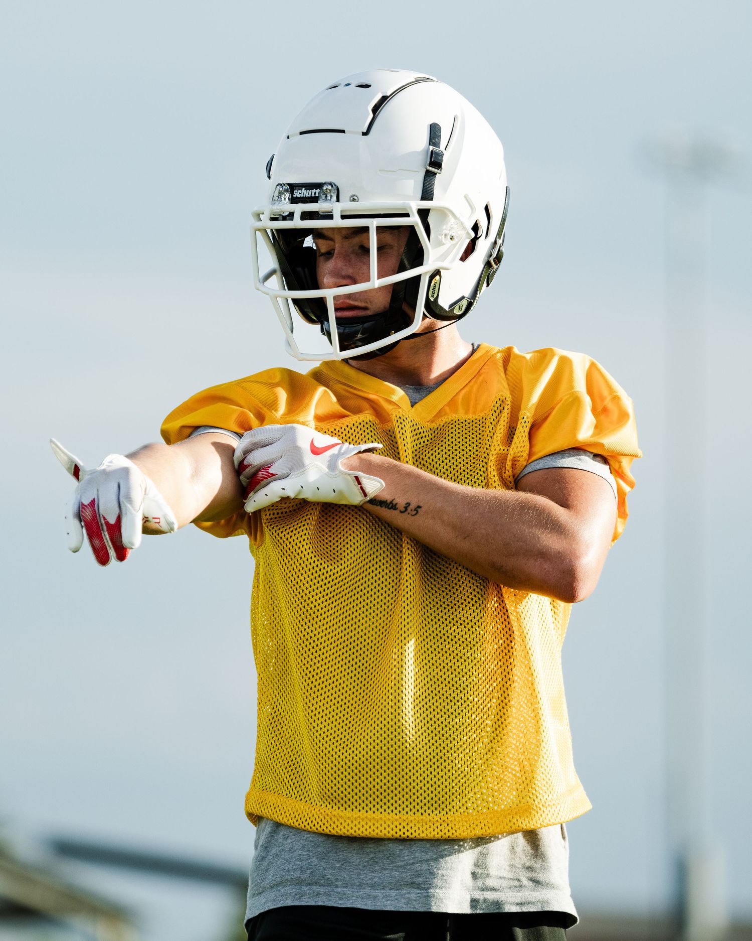 Football player in yellow jersey and white helmet adjusting gloves during practice.