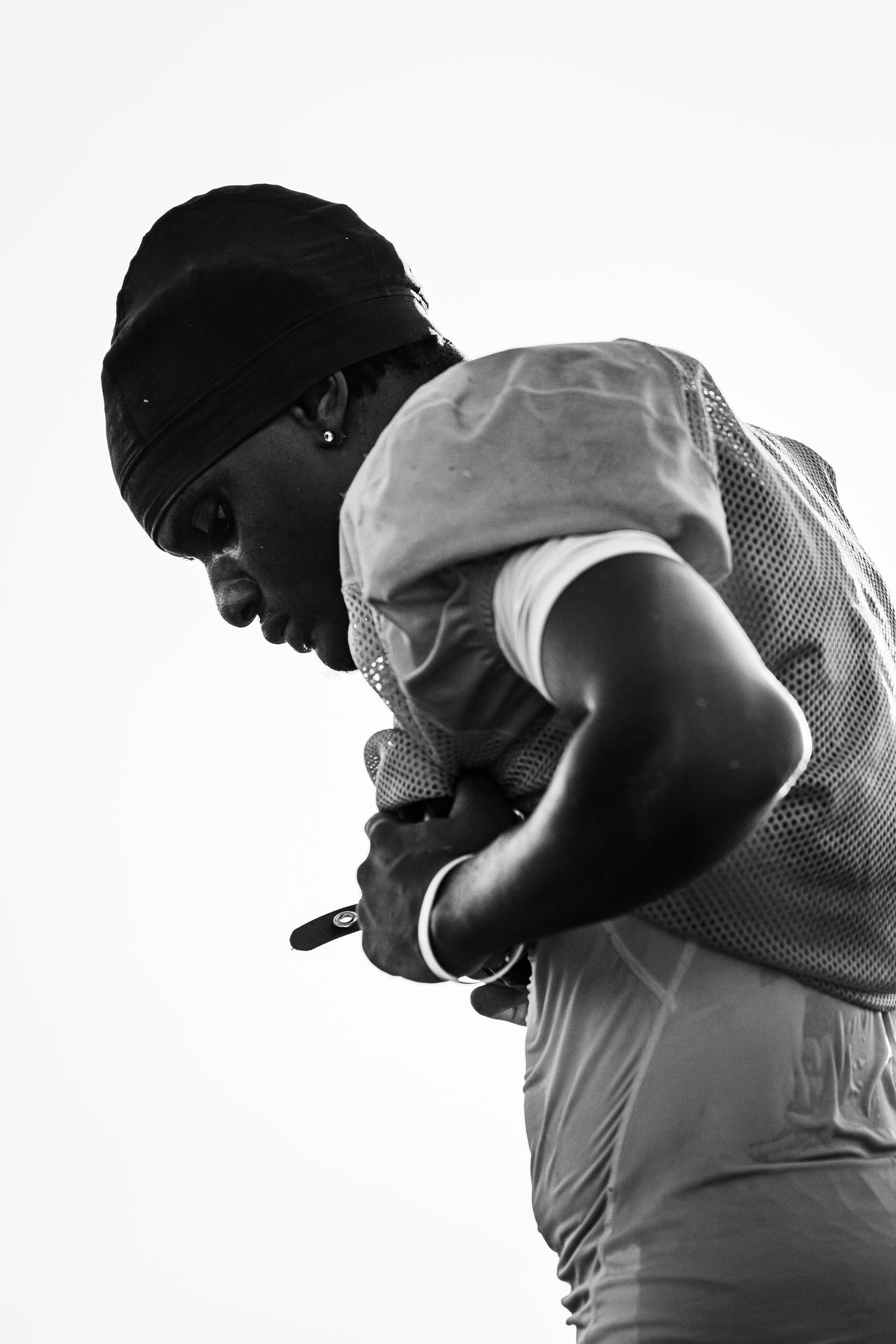 Black and white photo of a football player in jersey and beanie, looking down while holding a pen.