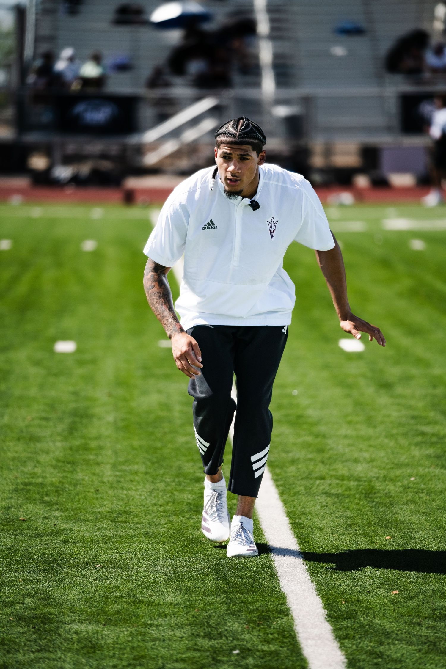 Arizona State University athlete in white Adidas shirt running on green turf field.