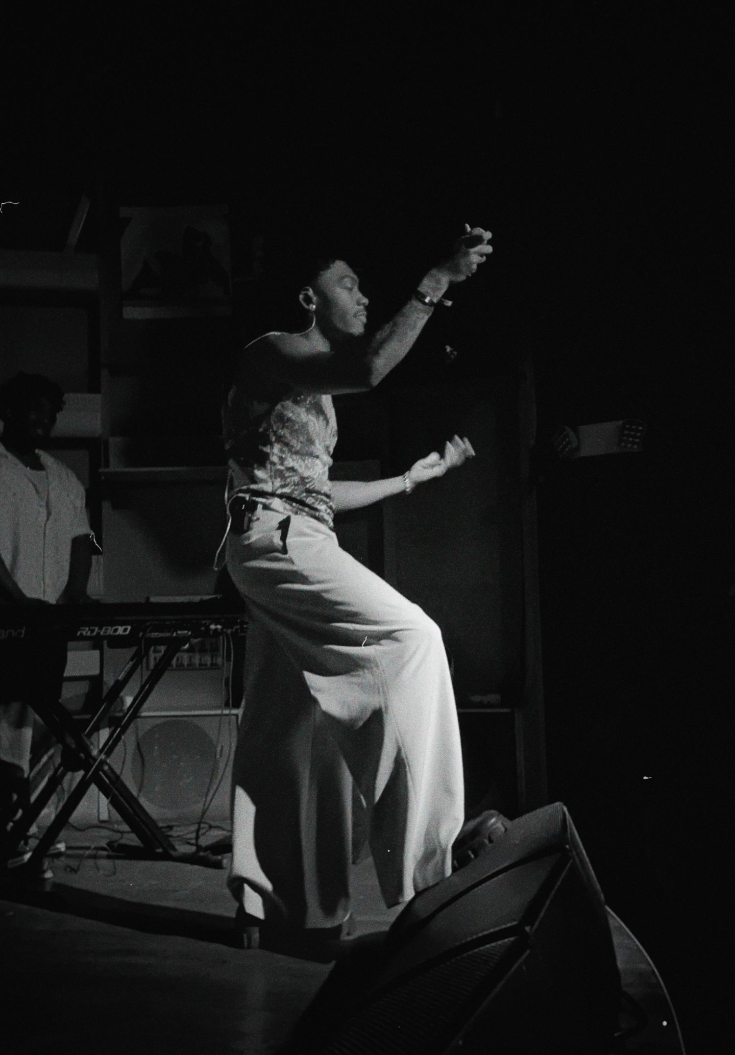 Black and white photo of a performer dancing energetically on stage with a keyboard player visible in the background.