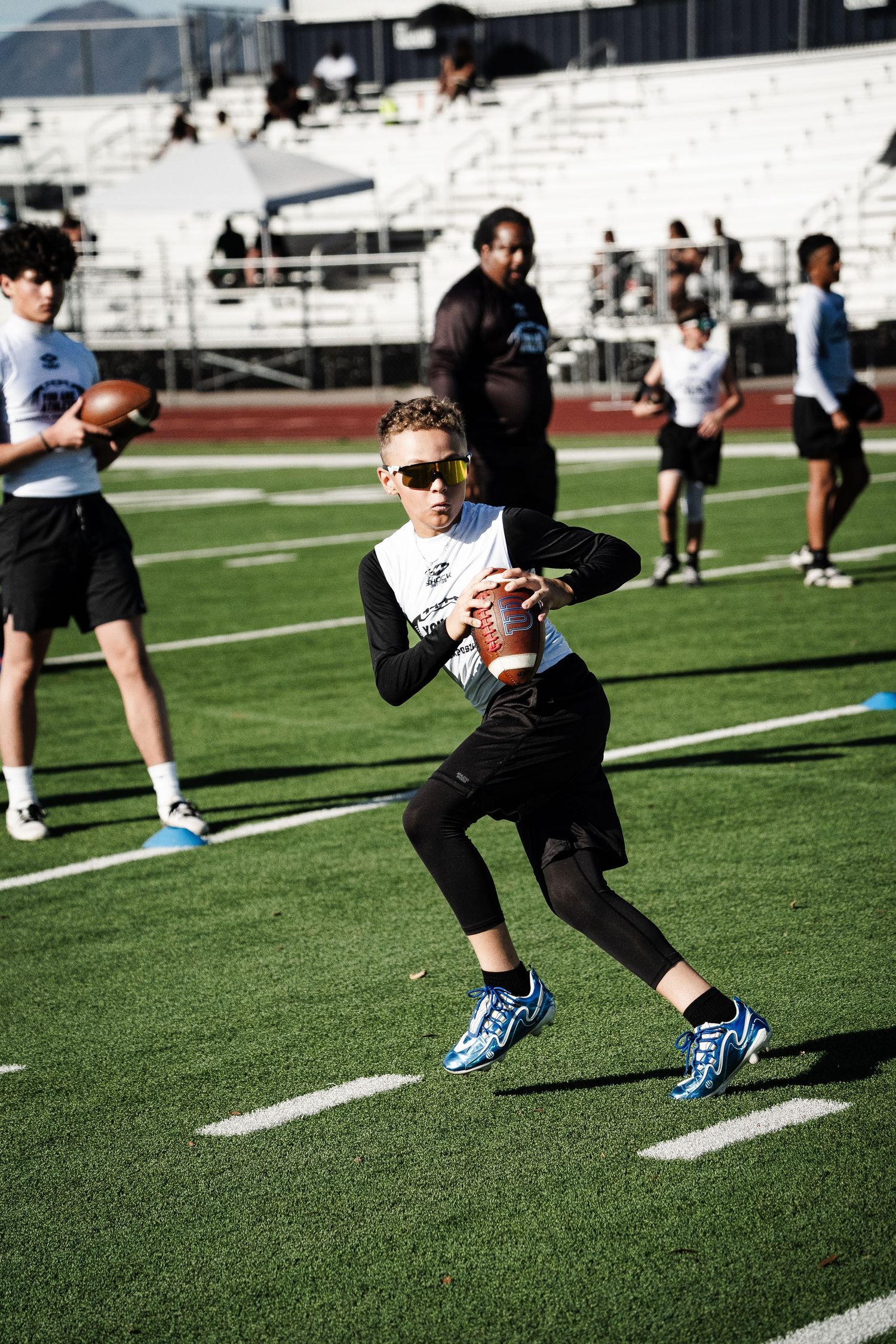 Youth quarterback in sunglasses preparing to throw football during outdoor practice session.