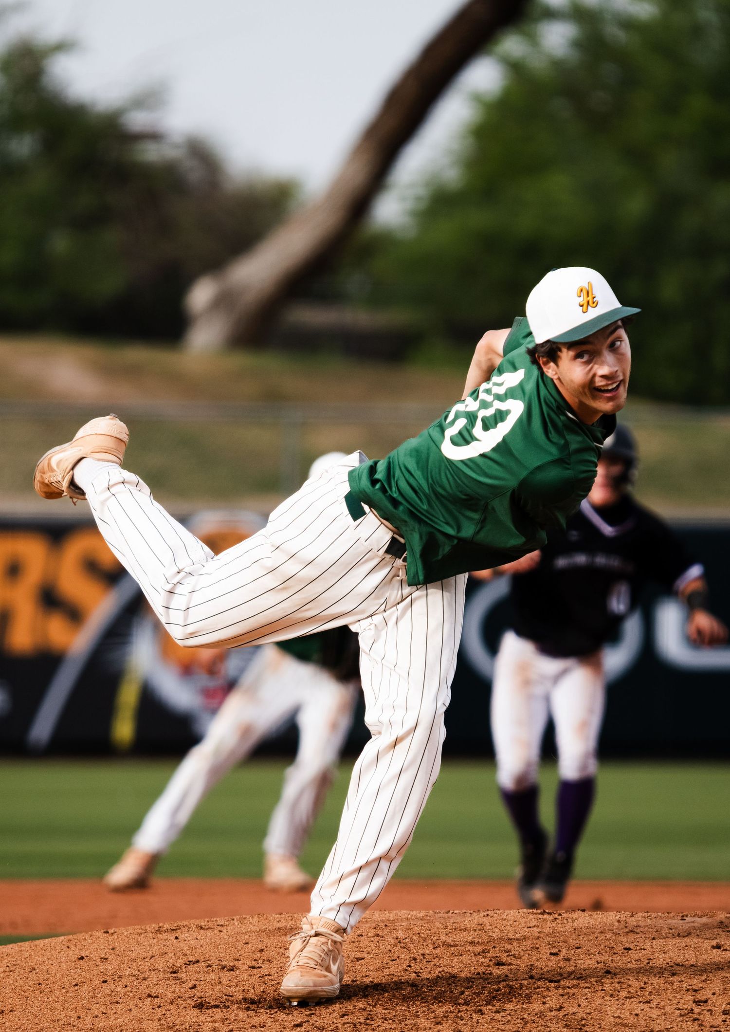 Baseball pitcher in green jersey mid-throw on mound.
