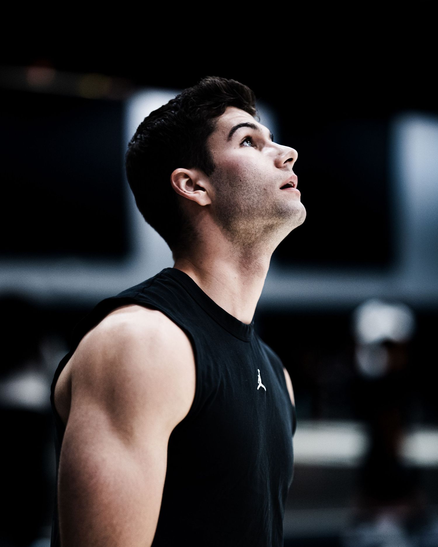 Athletic young man in black Jordan sleeveless shirt gazing upward in a gym setting.