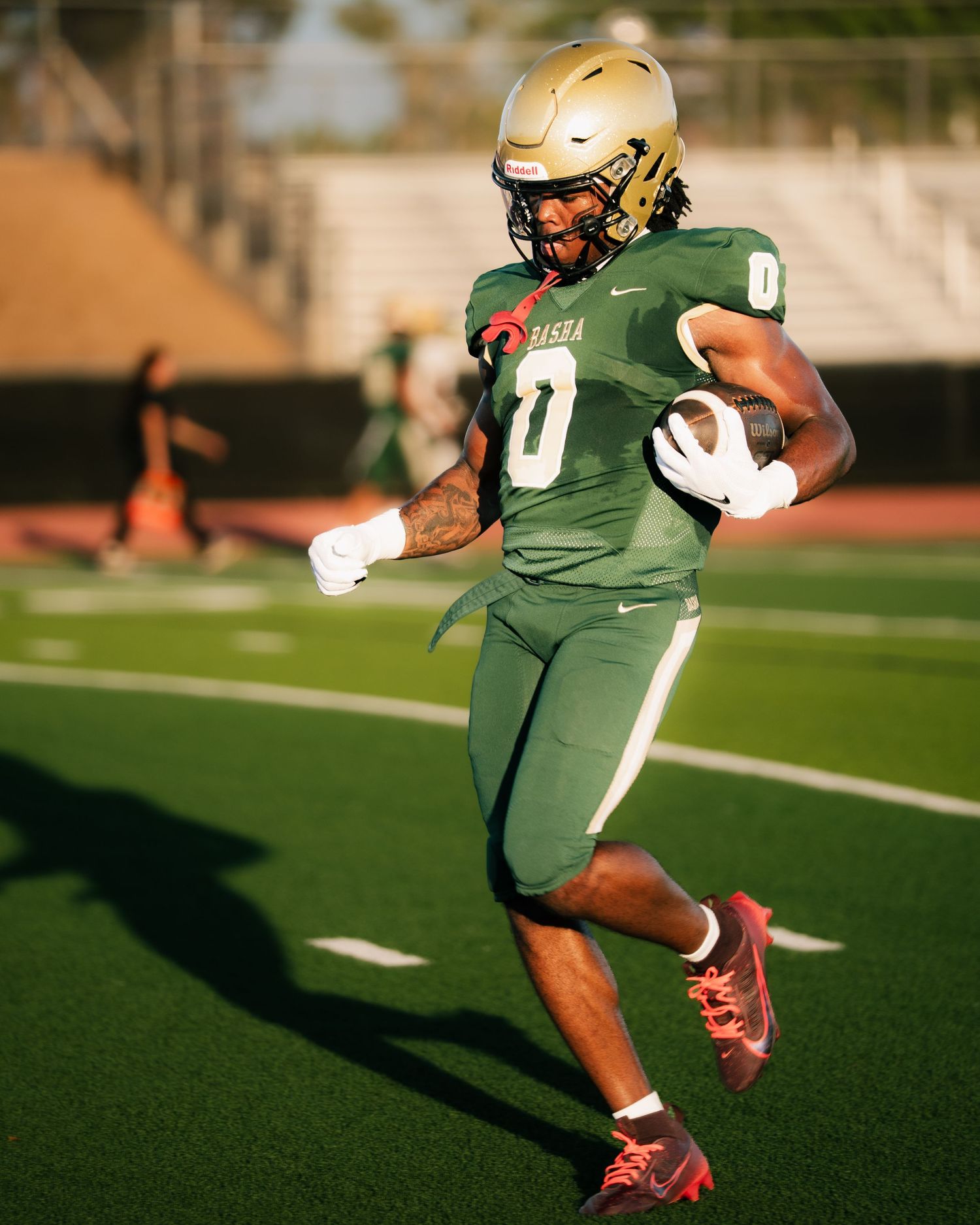 Football player in green uniform and gold helmet runs with the ball during a game on turf field.