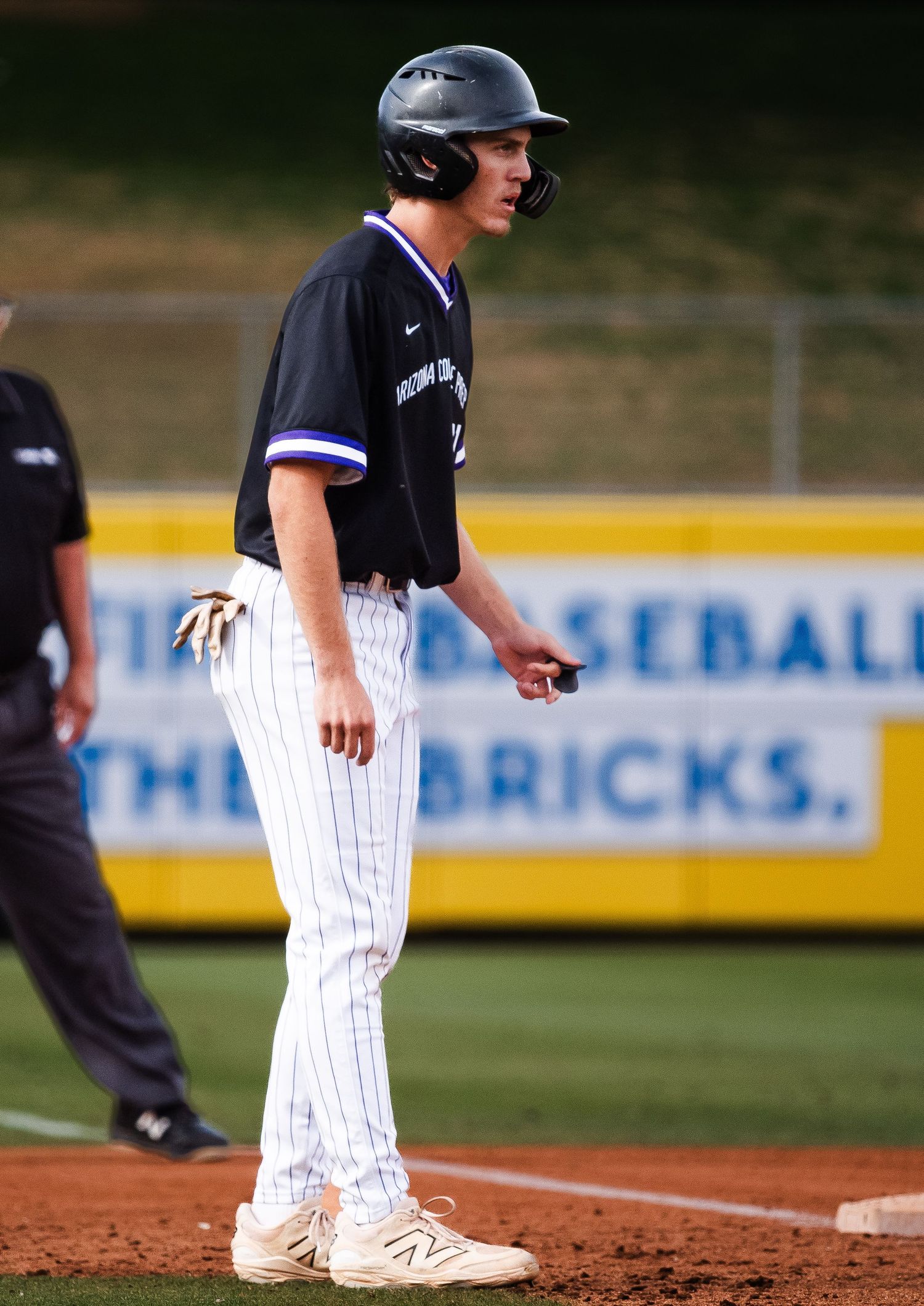 Young baseball player in black jersey and white pinstripe pants stands on base during a game.