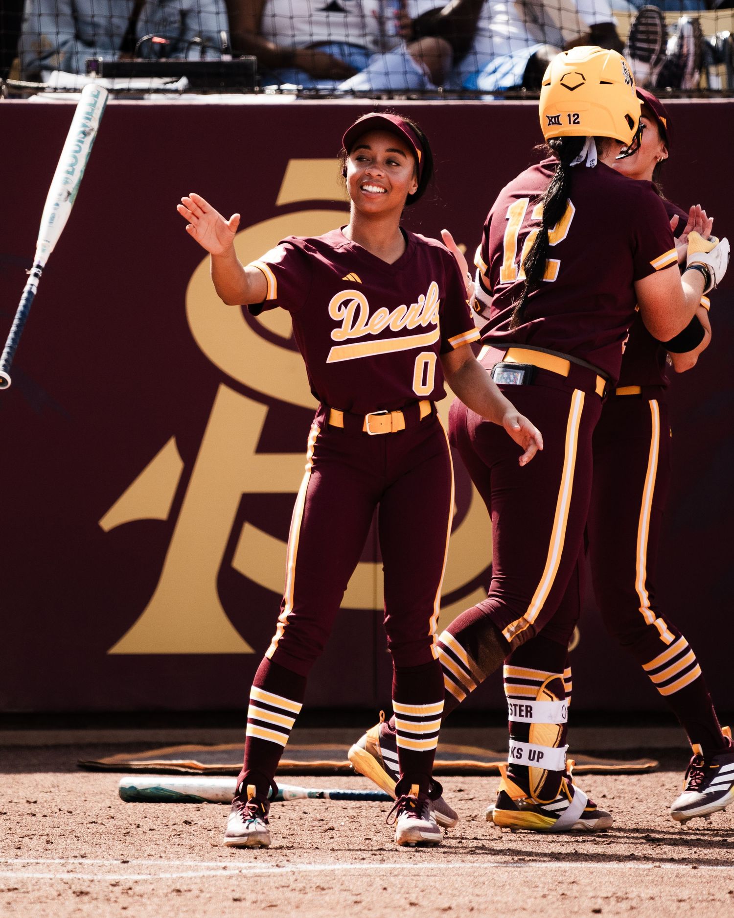 Arizona State Sun Devils softball player #0 celebrates with teammate during a game in maroon and gold uniforms.