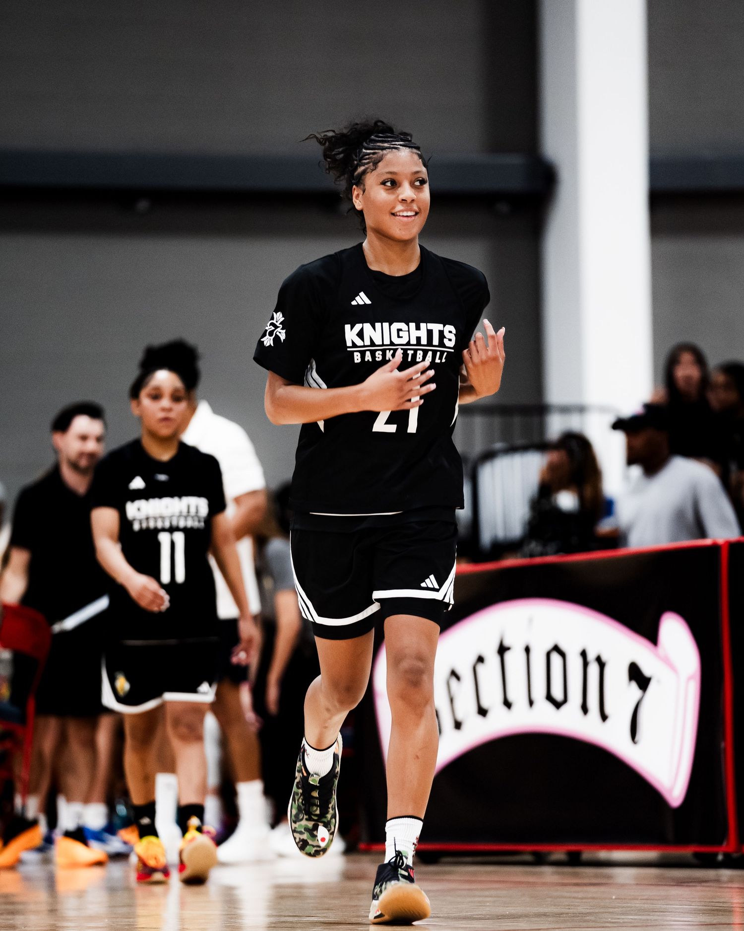 Female basketball player wearing Knights Basketball jersey number 21 jogging on indoor court during game.