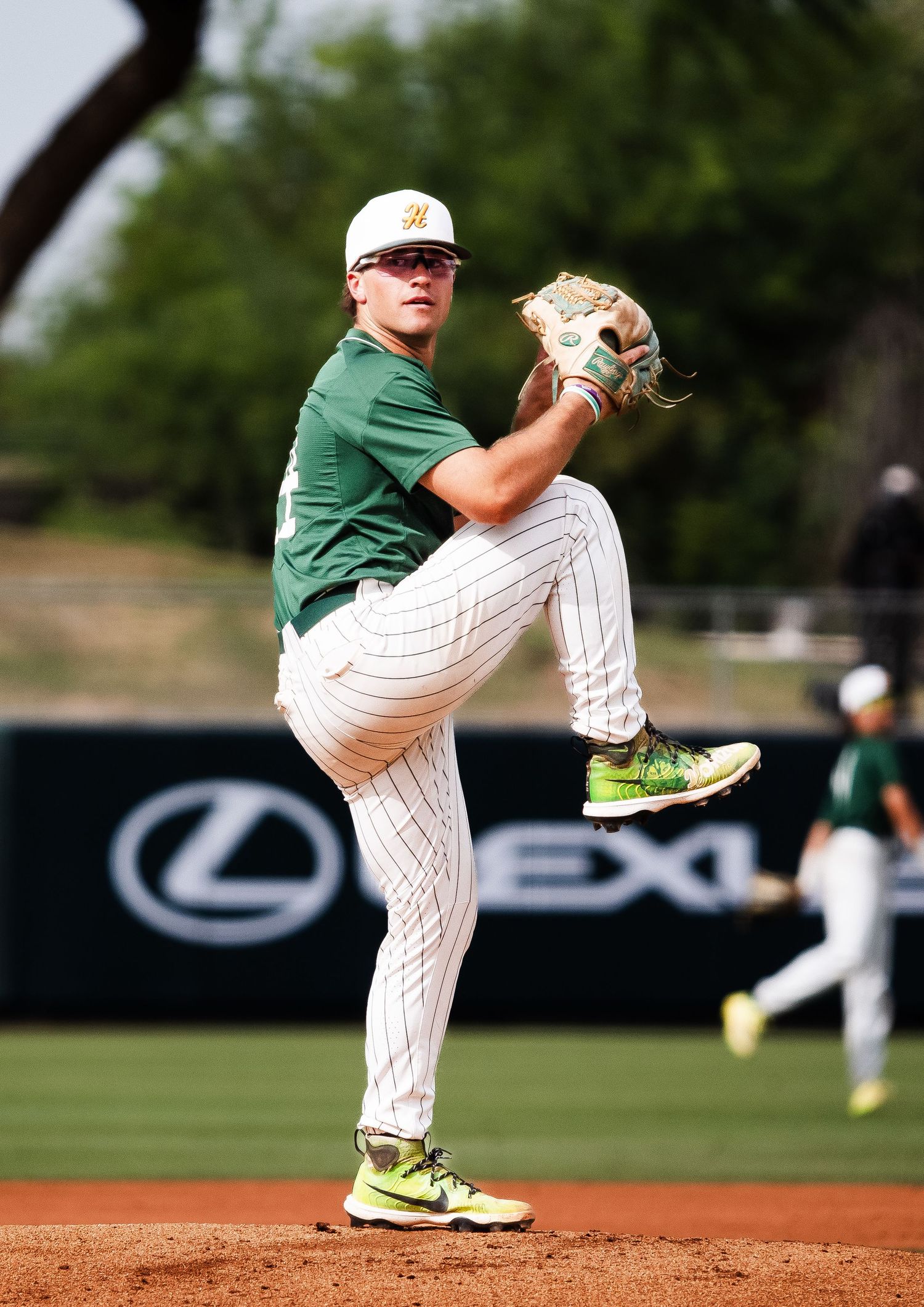 Baseball pitcher in green jersey winding up for delivery on mound.