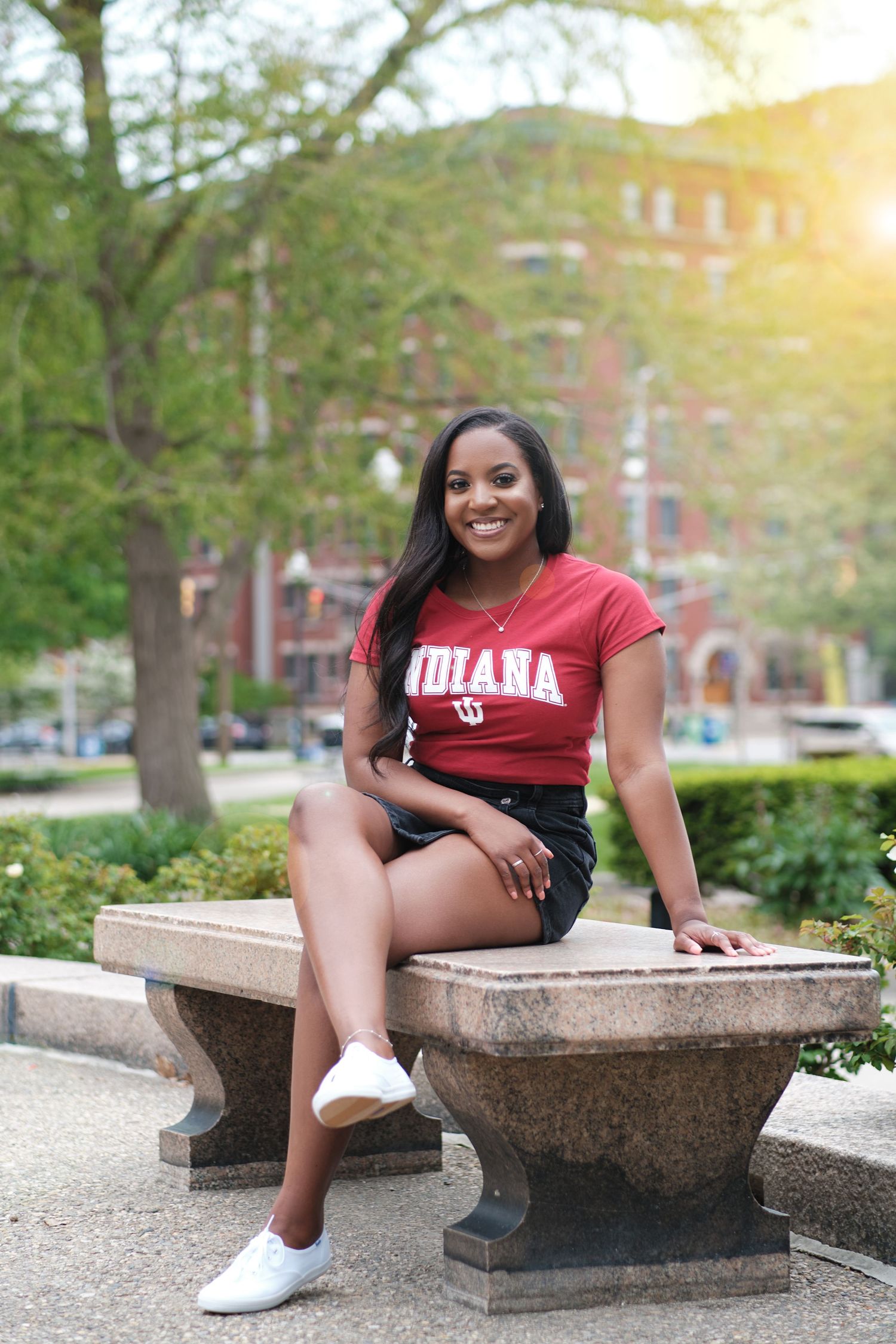 Smiling woman in Indiana University red shirt sitting on stone bench on campus.