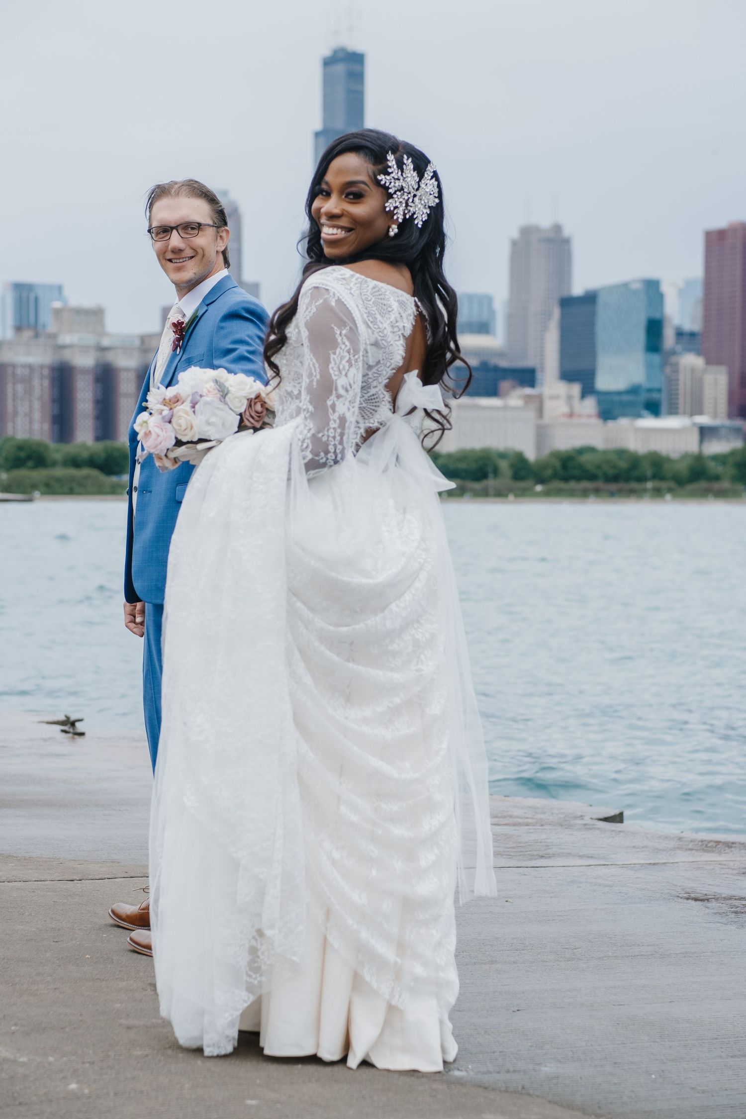 Bride and groom posing by the water with a soft Chicago skyline backdrop, captured in a timeless, modern portrait by Noelle Moss Photography