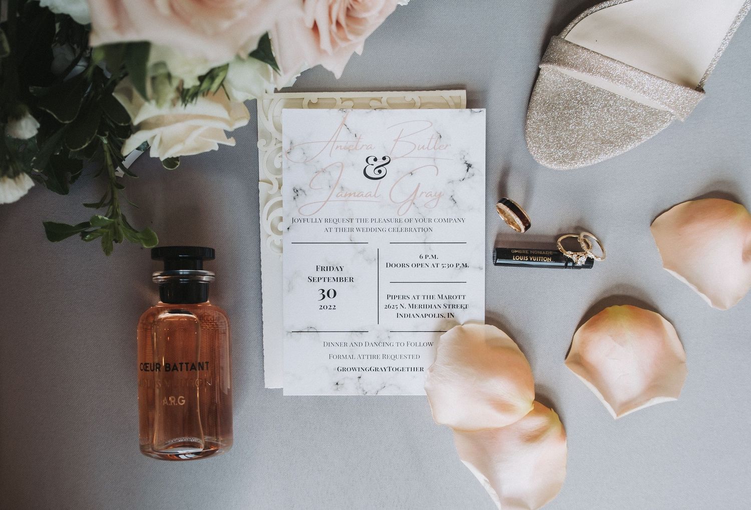 Wedding invitation flat lay with perfume, shoes, and floral details captured by Noelle Moss Photography