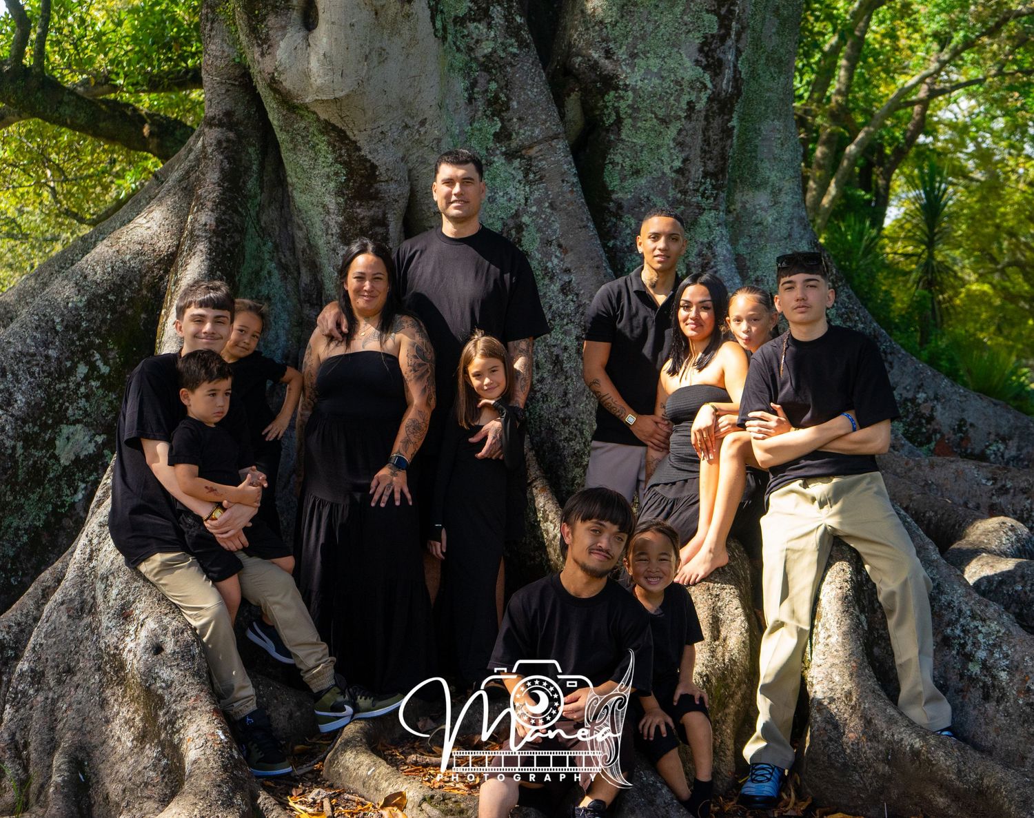 A large family group poses together in front of a massive ancient tree in a forest.