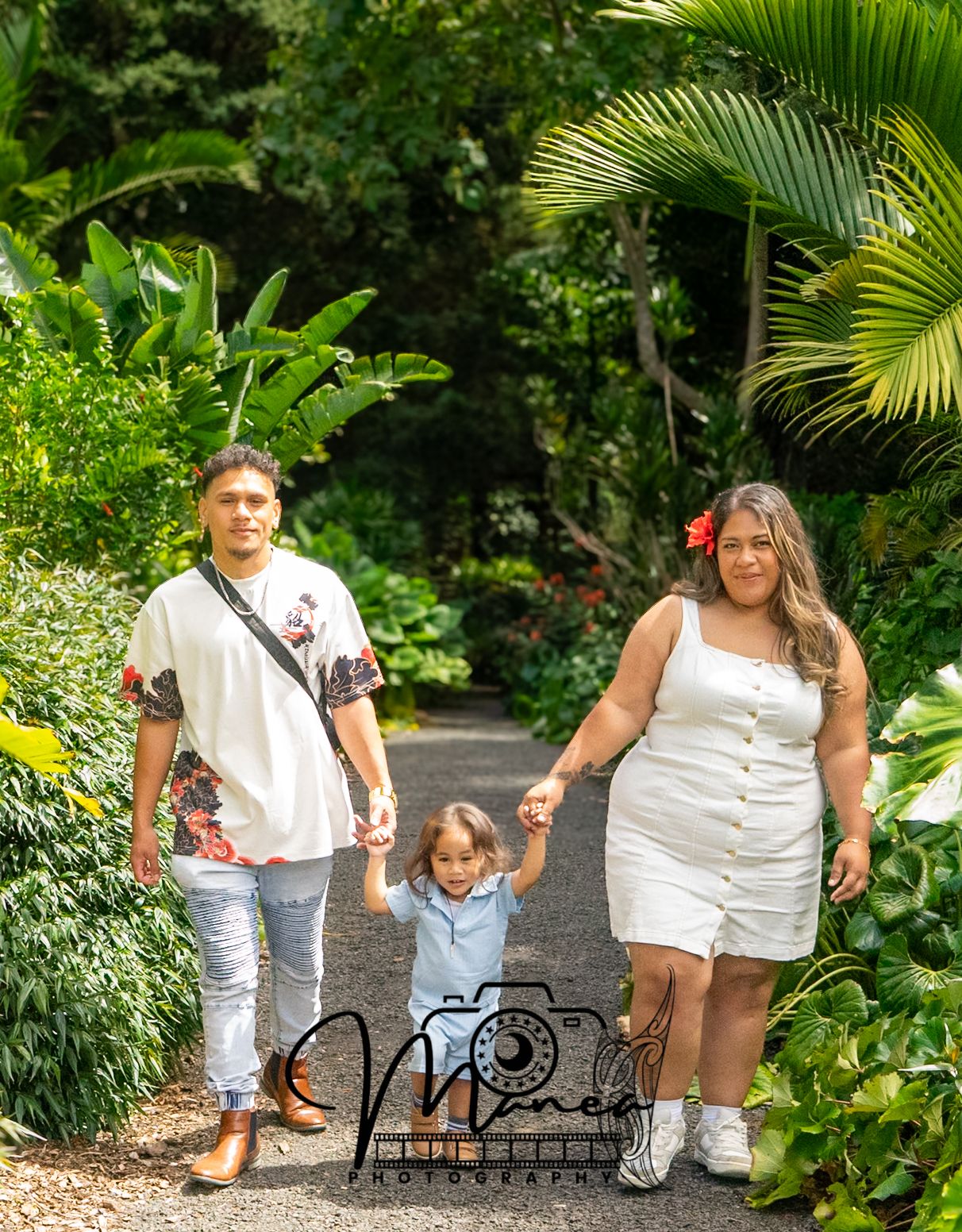 Young family of three walking hand in hand along a lush tropical garden pathway together.