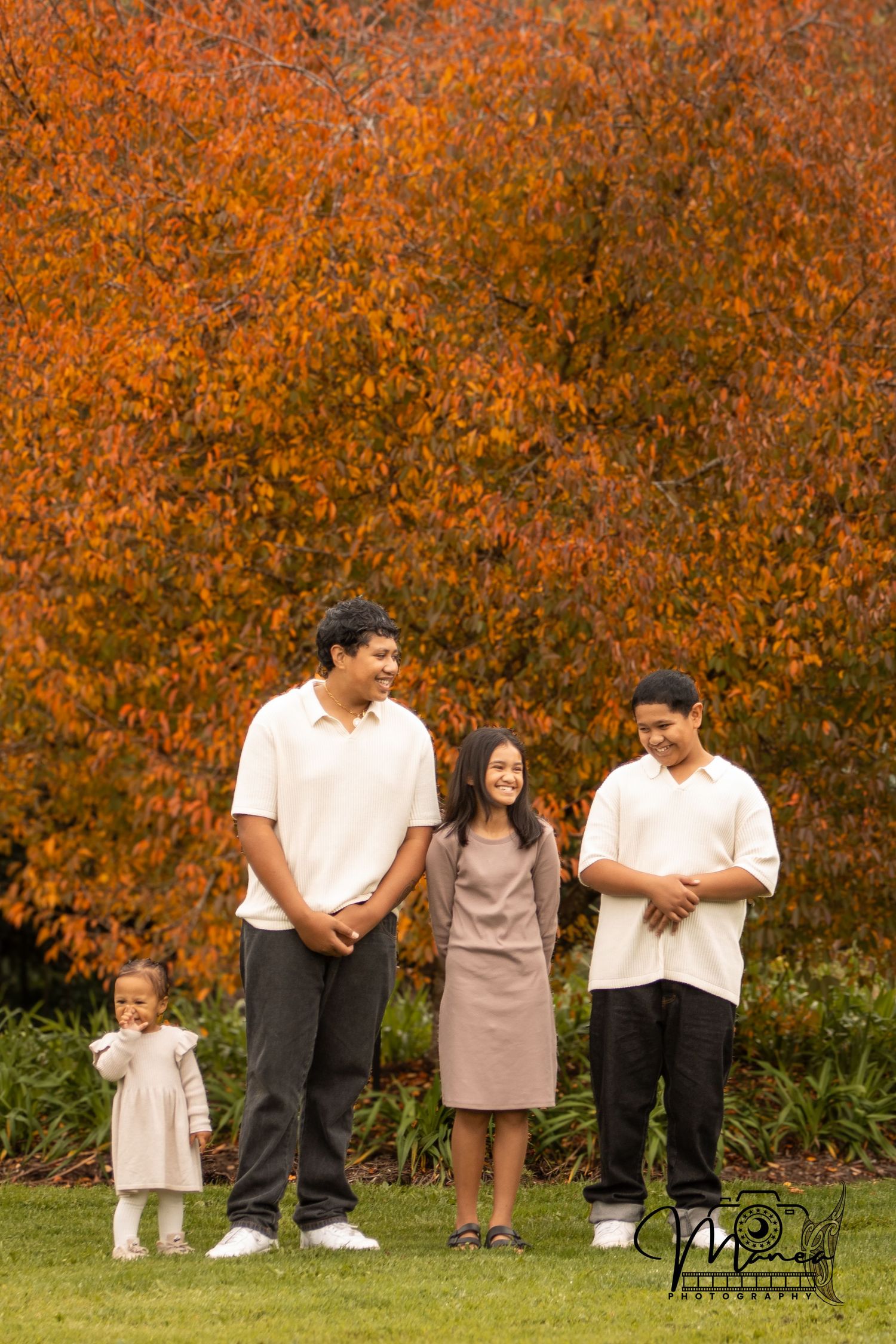 Four siblings posing together on a lawn with vibrant autumn orange foliage in the background.