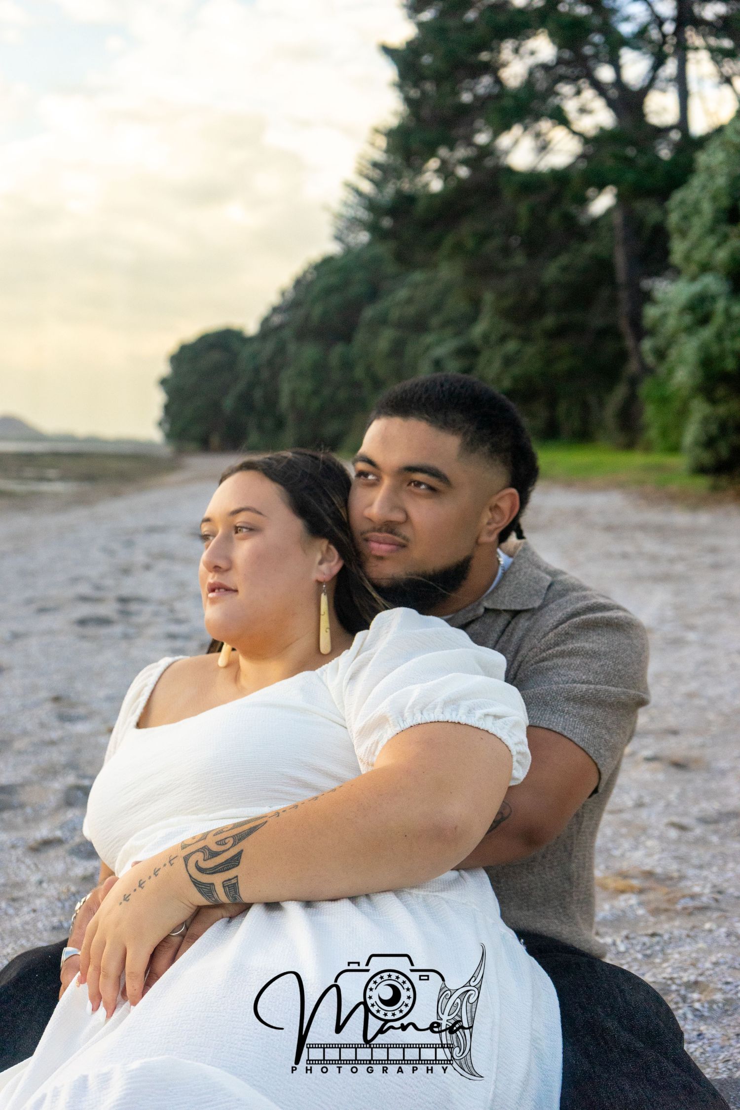 Couple sitting closely together on a pebble beach at dusk, gazing into the distance peacefully.