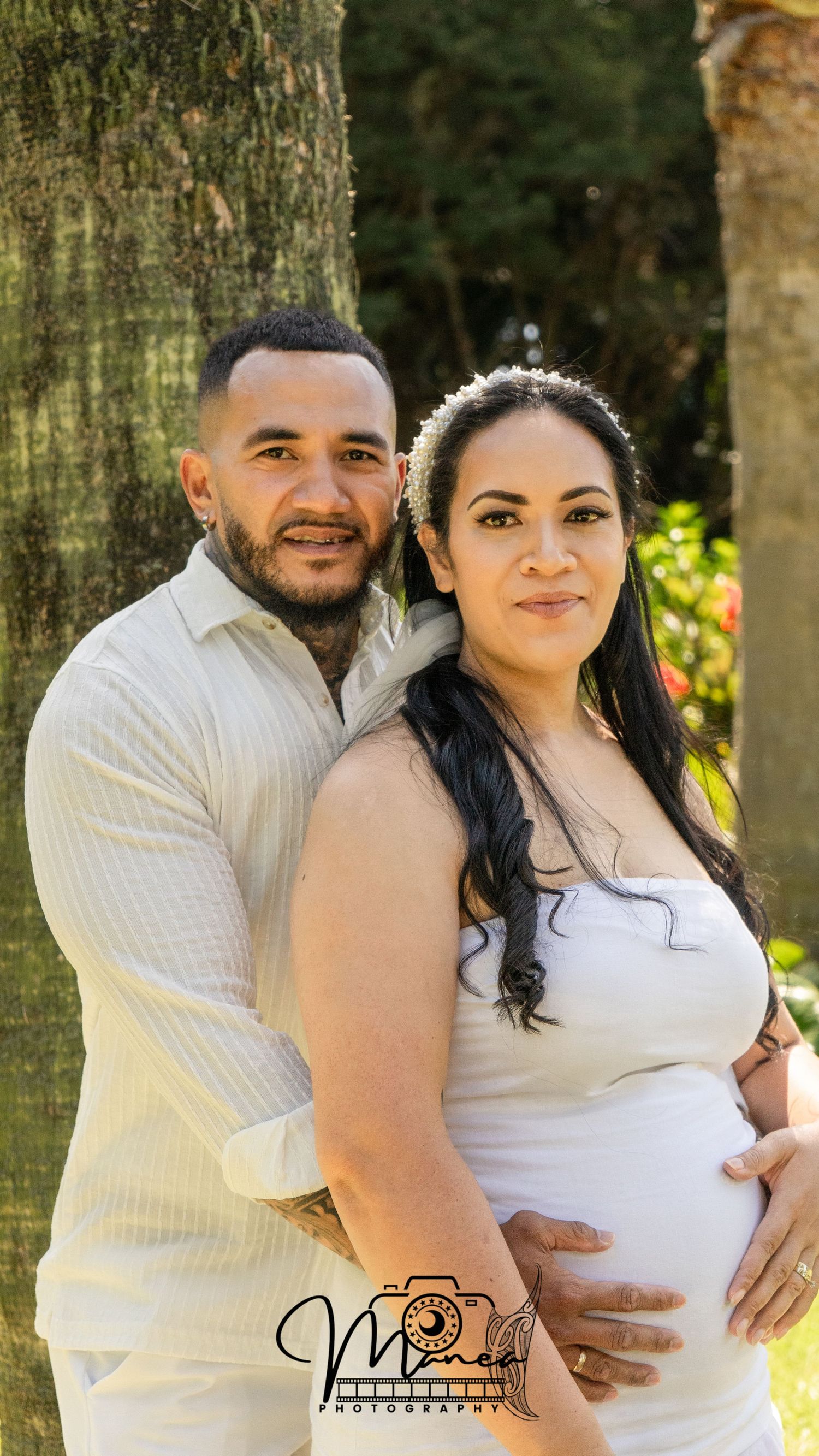 Expecting couple posing together outdoors near tree trunk for maternity photo session.