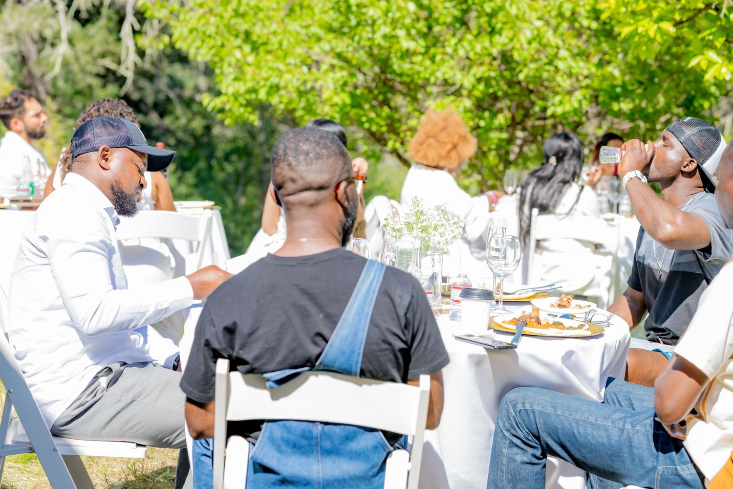 Group of people seated at an elegant outdoor dining table enjoying a sunny garden party event.