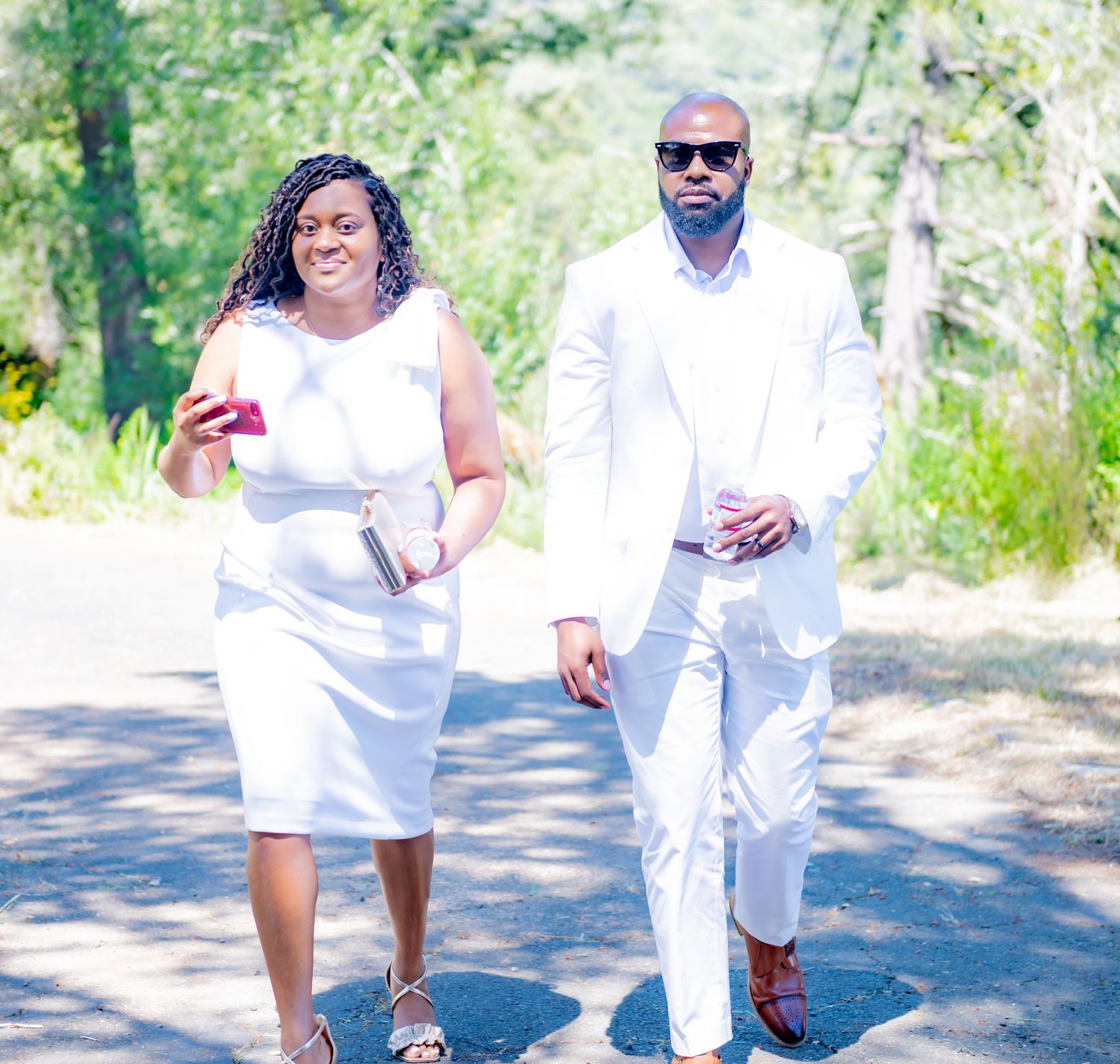 Couple dressed in white walking together on a sunny outdoor path.