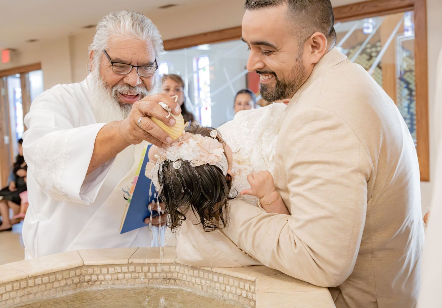 A priest pours water over a person's head during a Catholic baptism ceremony at a church font.