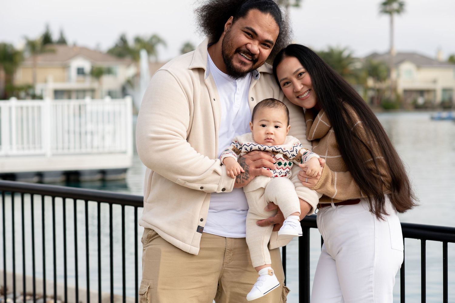 Young couple holding their baby together outdoors near a scenic waterfront location.