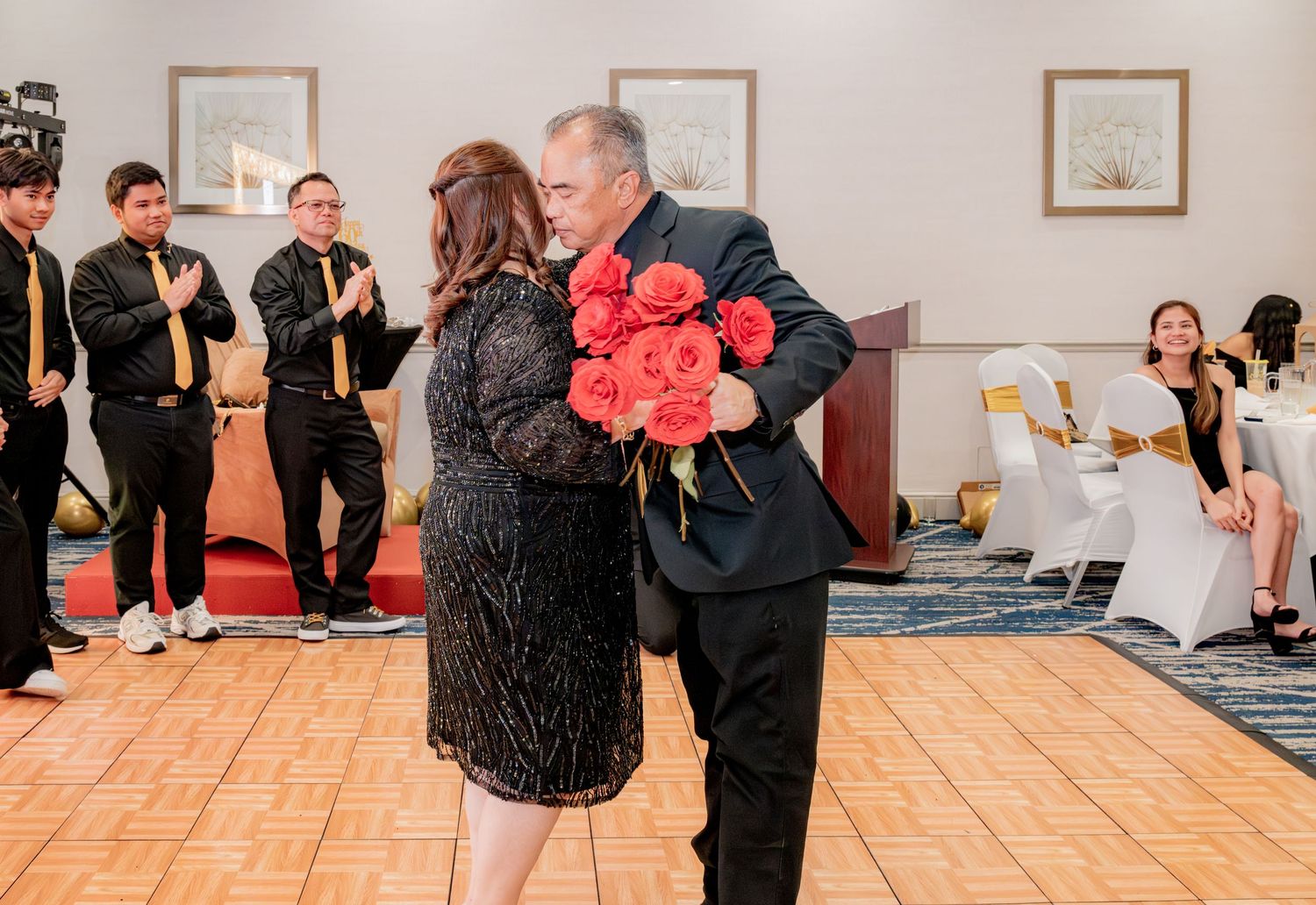 Couple sharing a romantic dance while man presents red roses at a 60th birthday celebration.