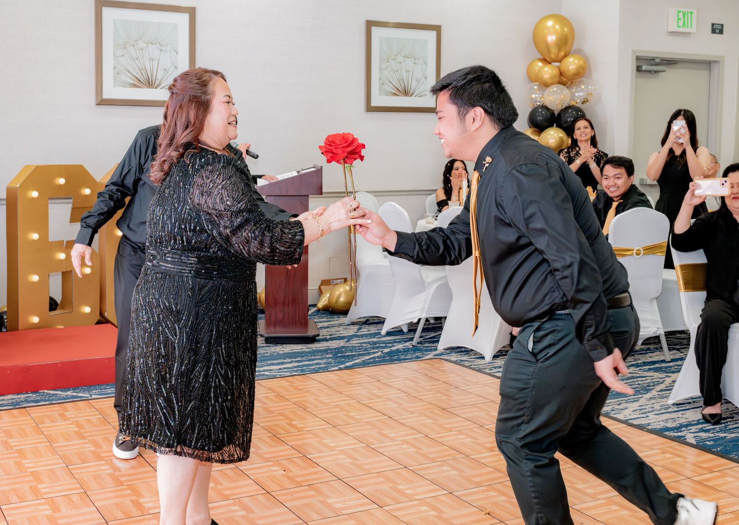 Man presenting red rose to woman on dance floor at festive birthday party.