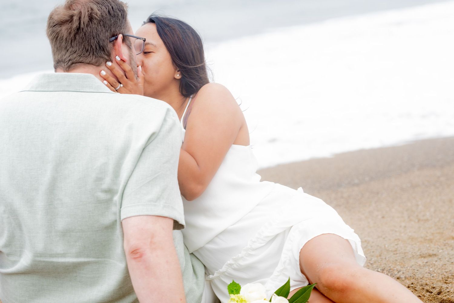Couple sharing a romantic kiss while sitting together on the sandy shore of Baker Beach.