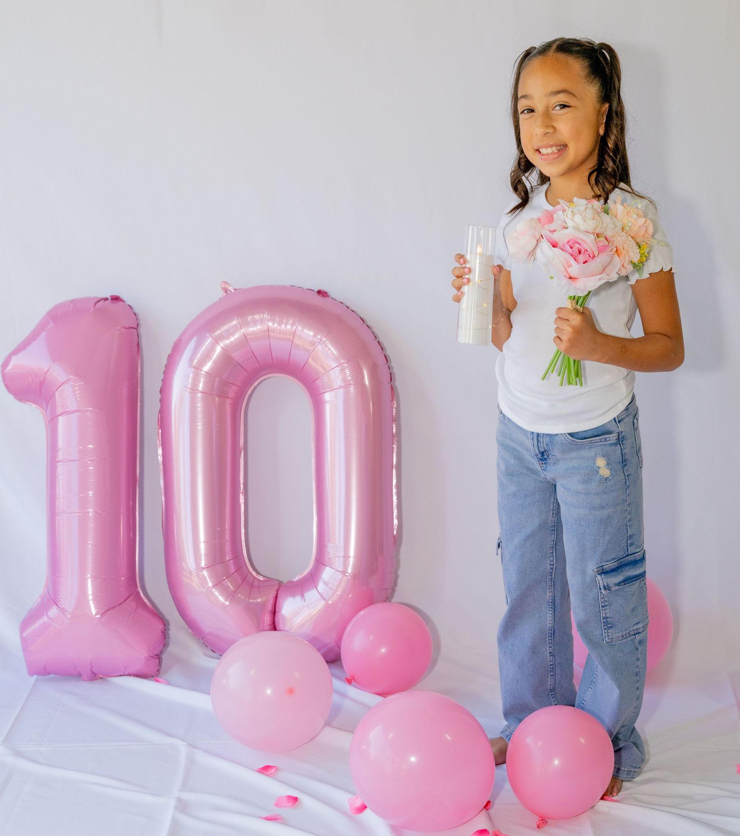 Girl celebrates 10th birthday holding flowers beside large pink number 10 balloon.