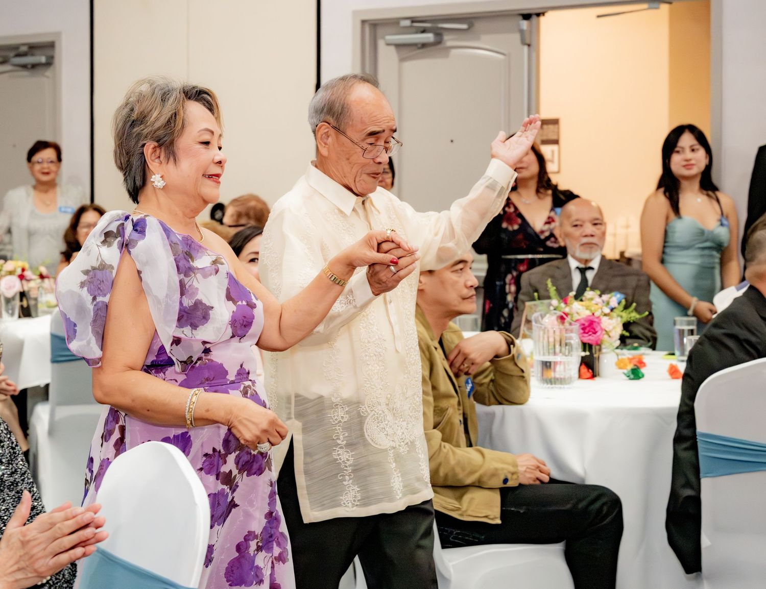 Elderly couple dancing together at a formal banquet event in a decorated hall.