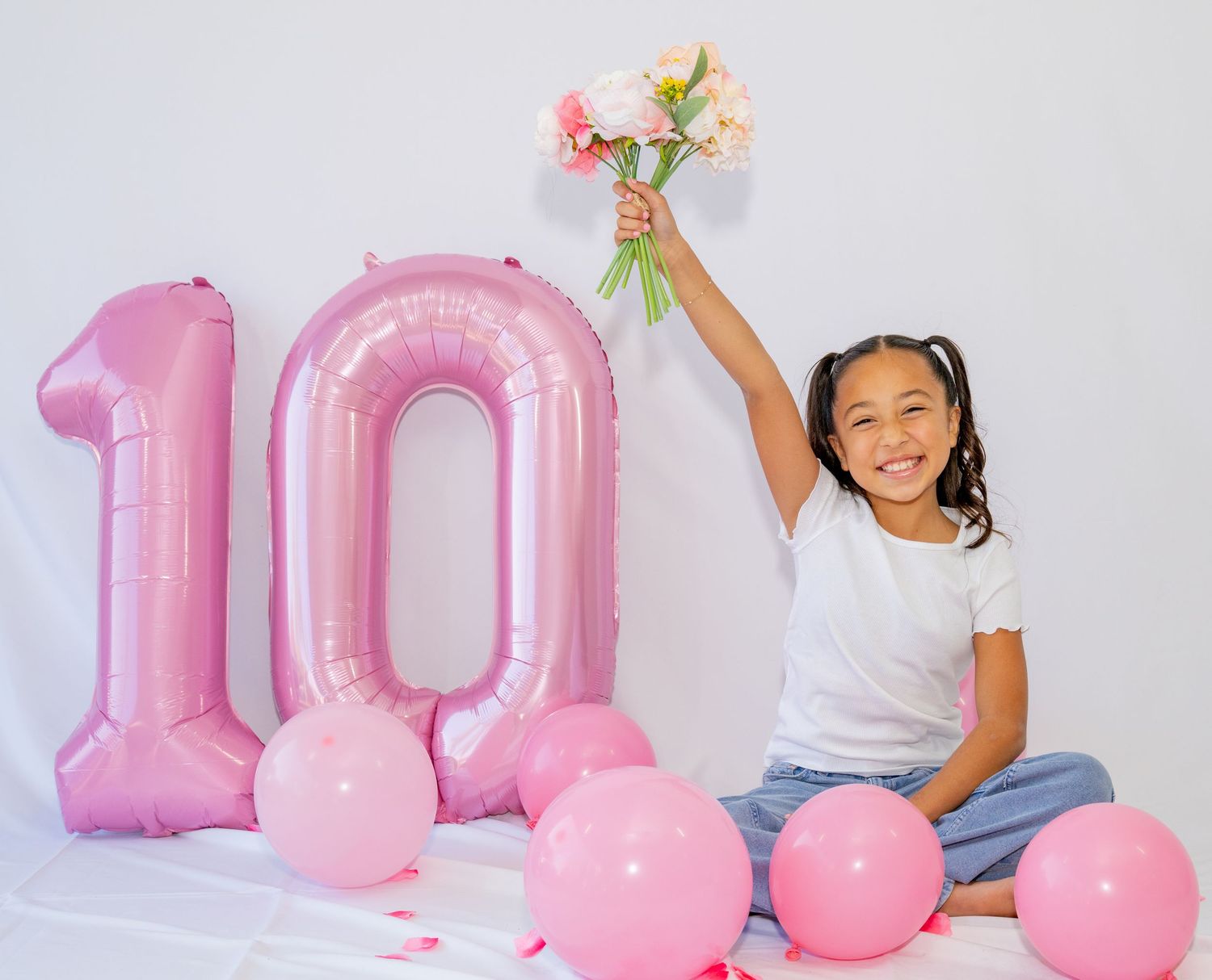 Smiling girl raises pink flower bouquet beside large pink number 10 birthday balloon.