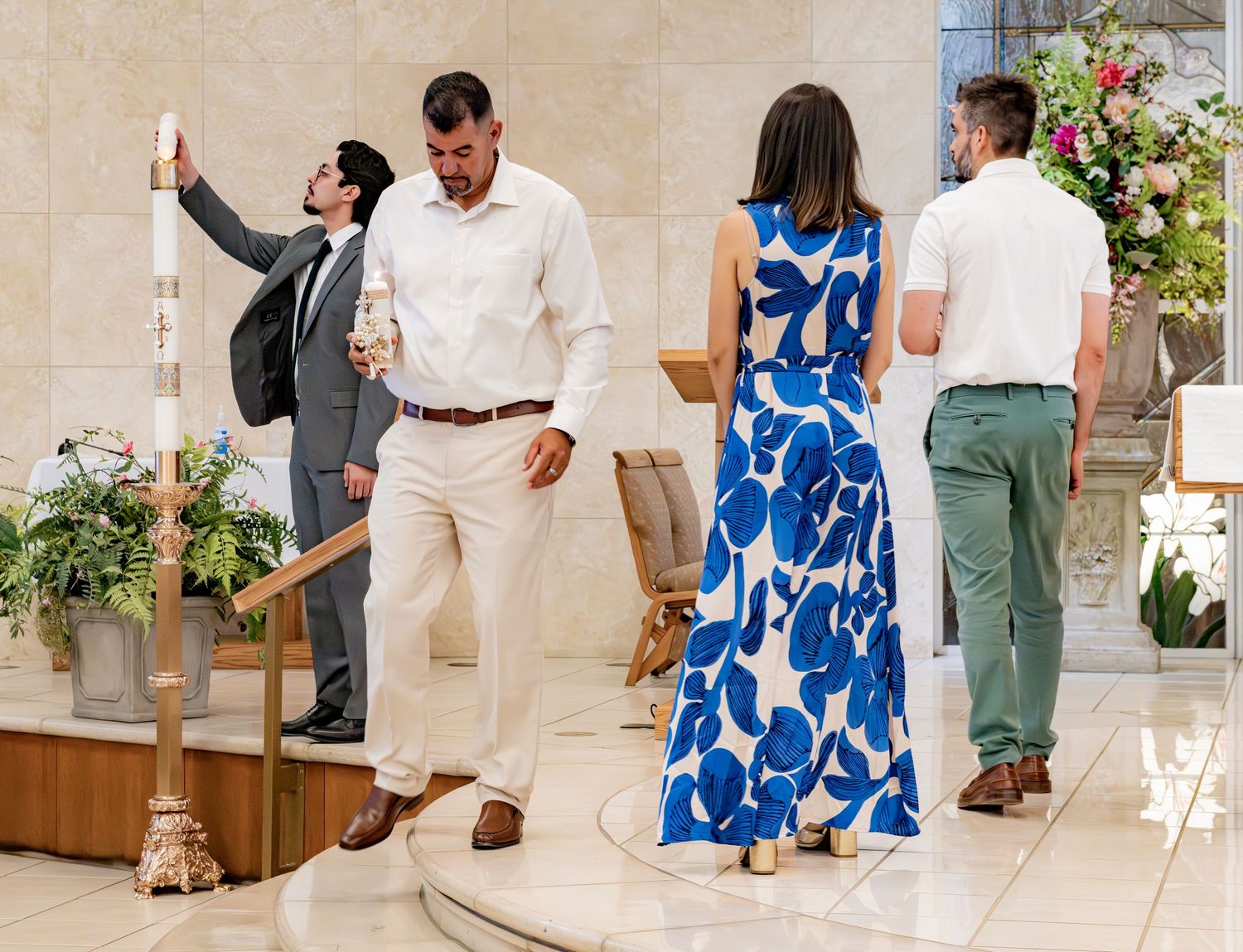Guests and wedding party gather around a tall candle during a church baptism ceremony.