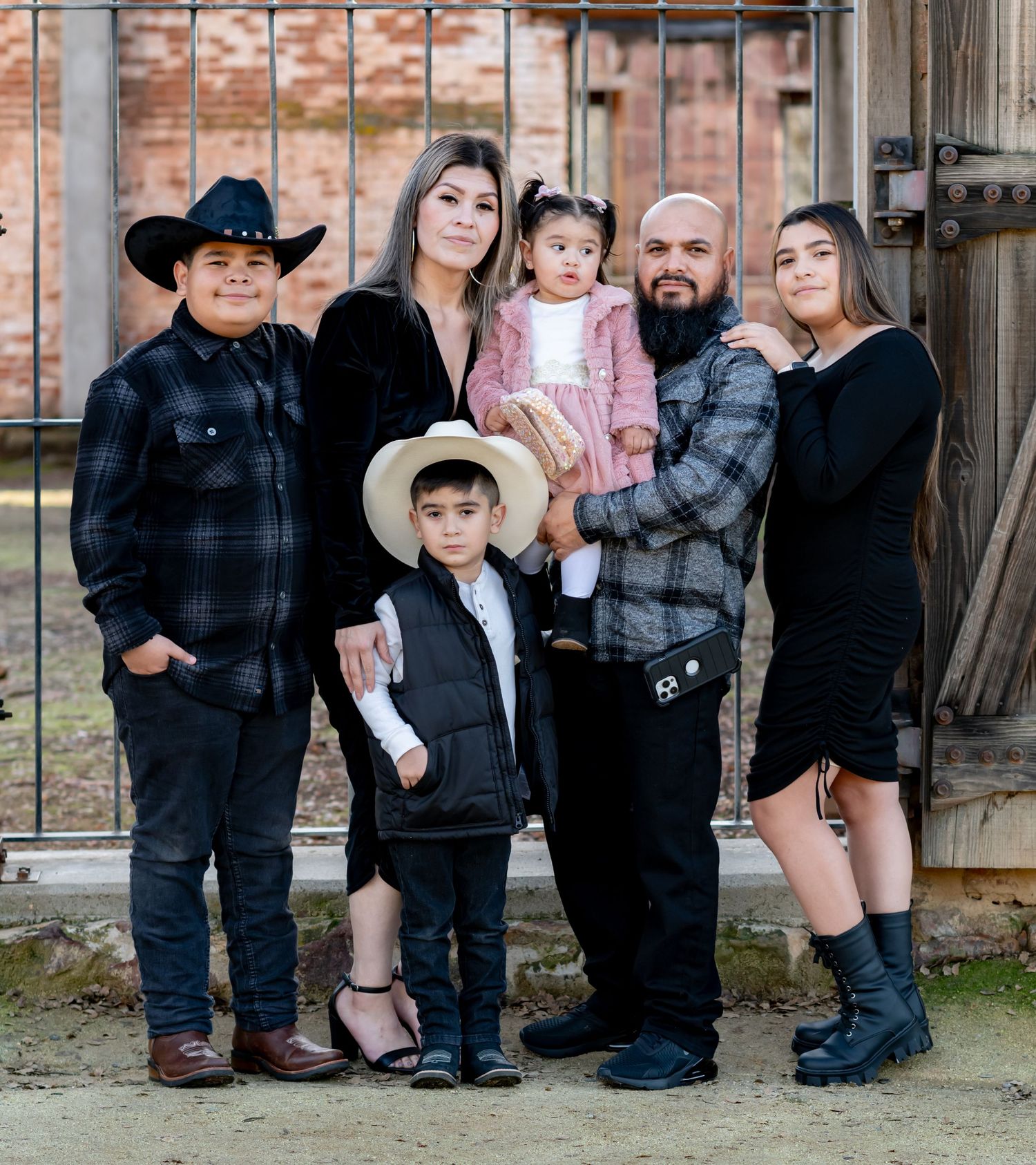 Family of six posing together in coordinated black and plaid outfits near a rustic barn.
