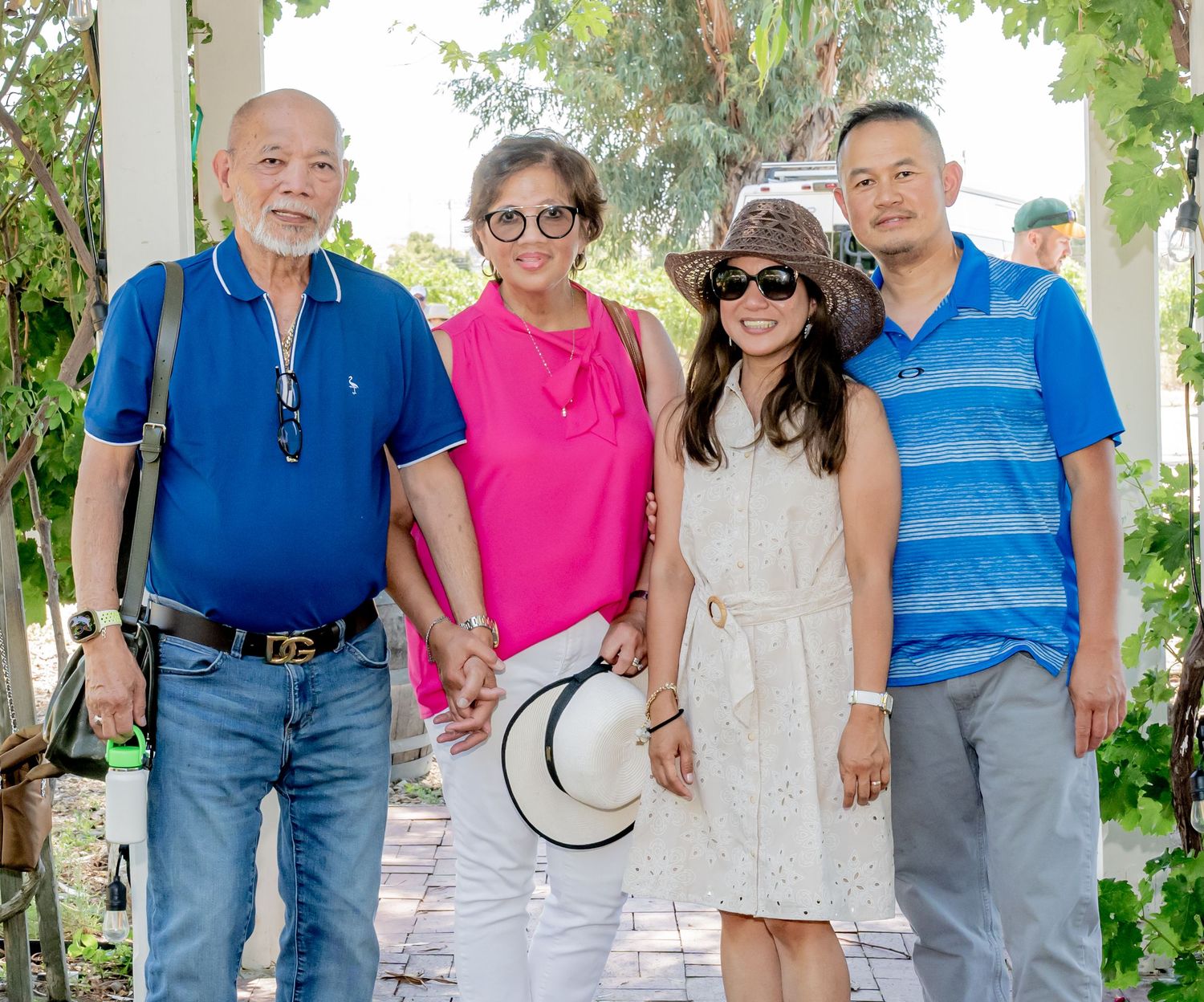 Four people posing together outdoors on a sunny day, dressed in colorful casual attire near green trees.