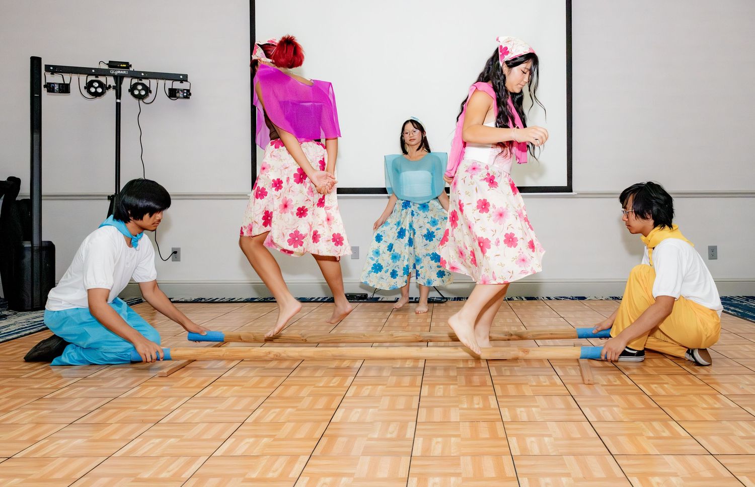 Traditional Filipino Tinikling bamboo dance performance with colorful floral dresses and dancers stepping between poles.