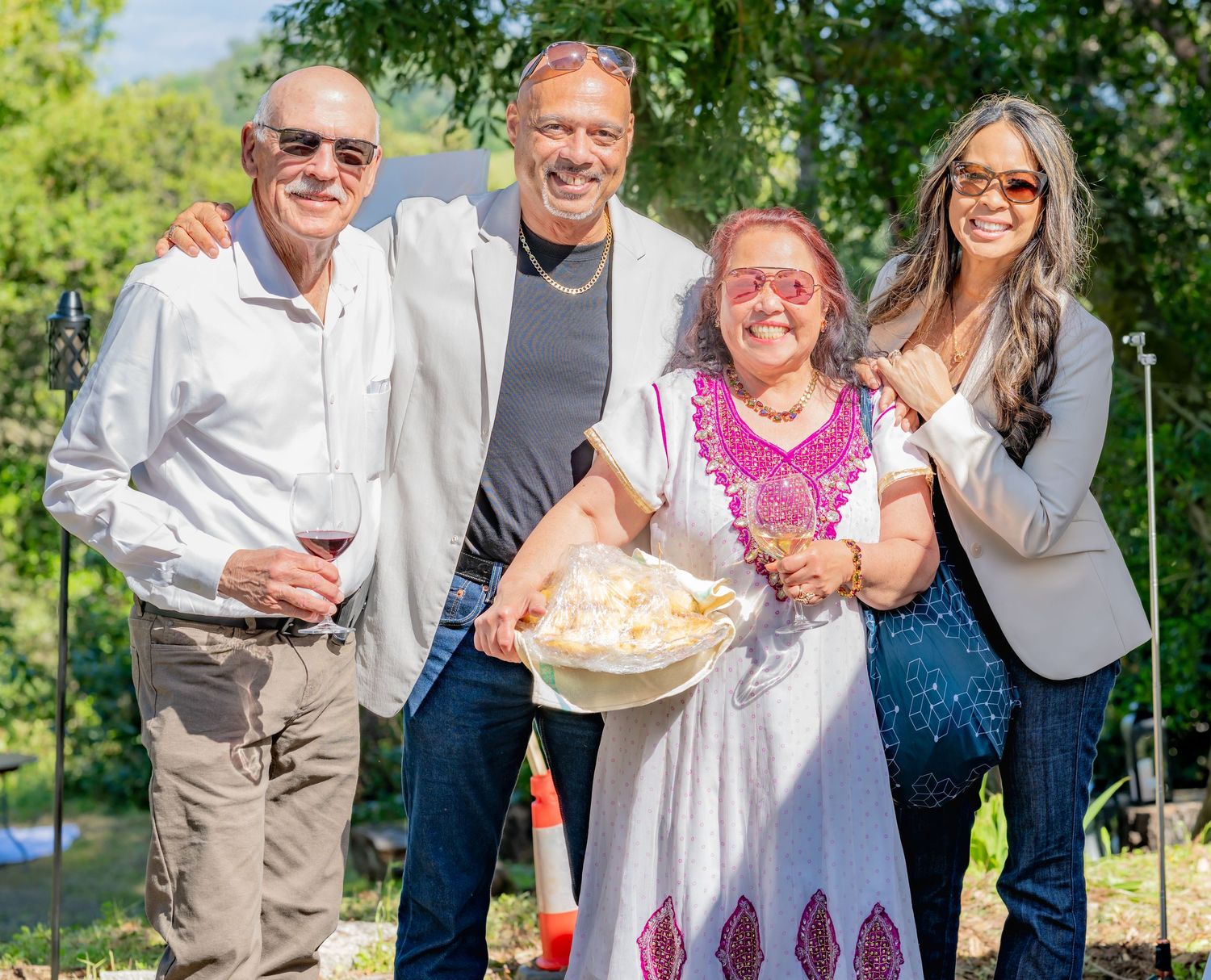 Four people smiling together outdoors, one holding a bowl of food.