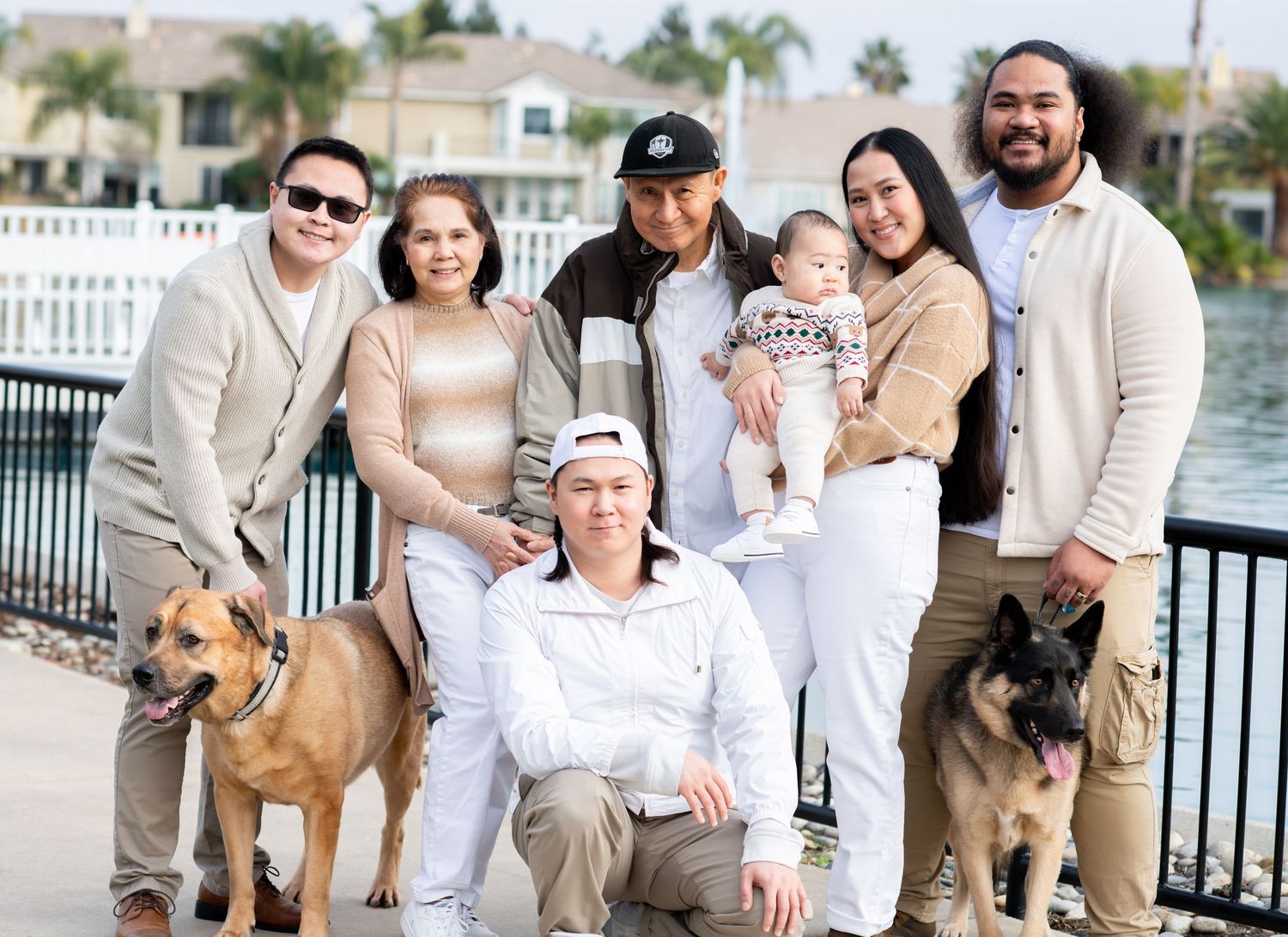 Extended family group of seven posing outdoors near a waterfront with two dogs.