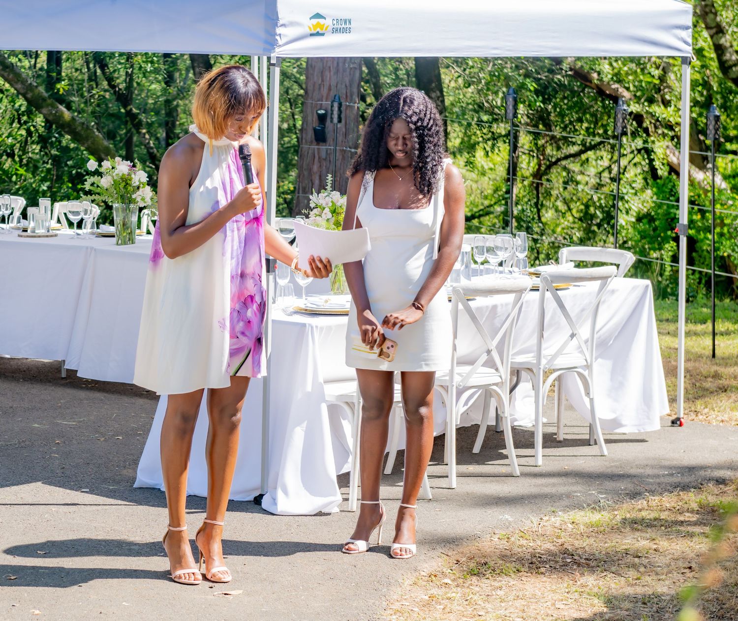 Two women in white dresses conversing at an outdoor event venue.