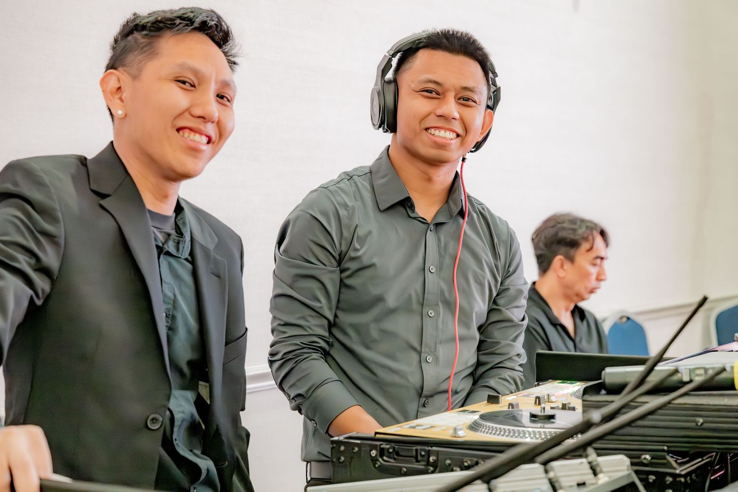 Two men smiling at a DJ booth during an event.