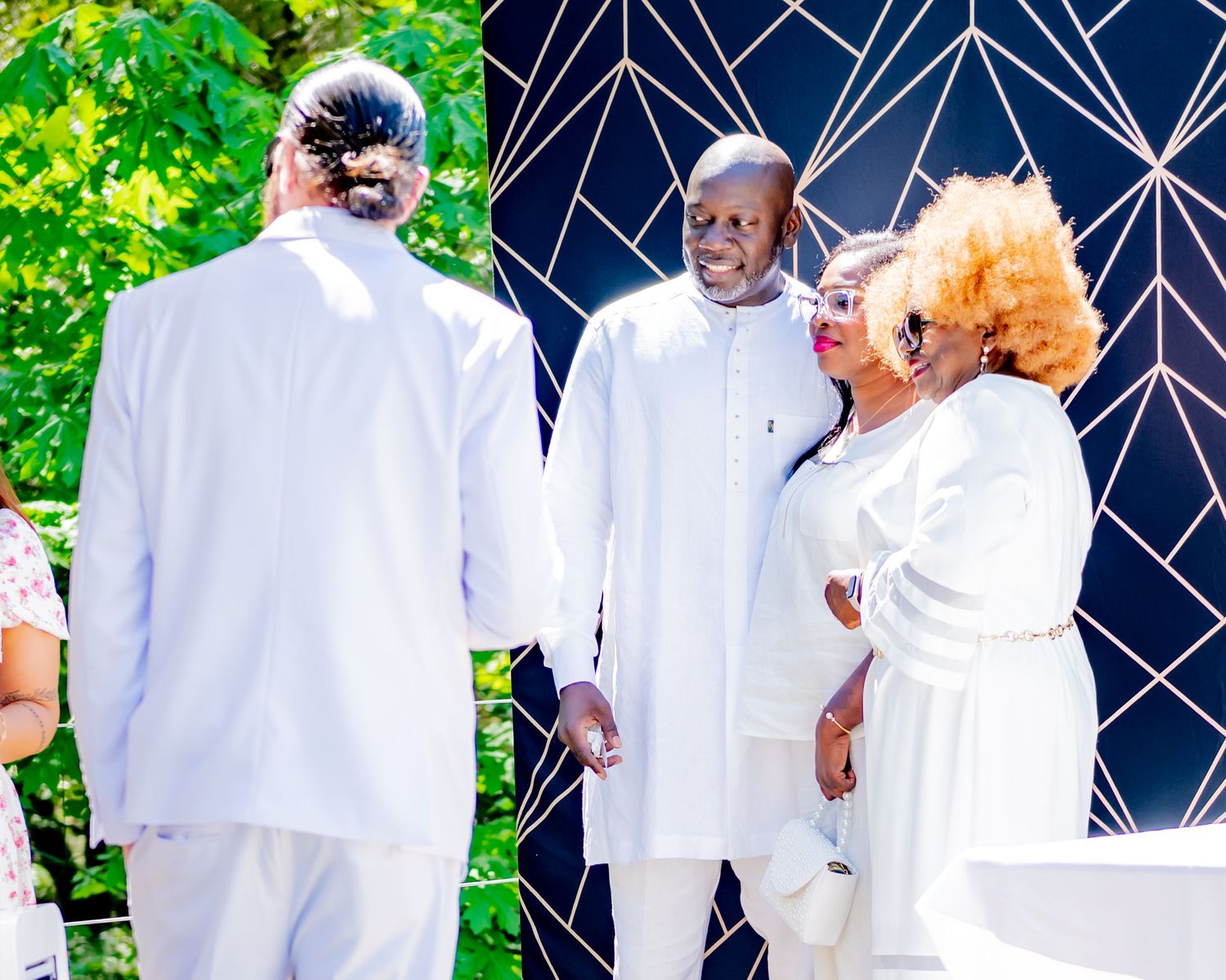 Three guests in white attire conversing outdoors near a geometric black and white decorative backdrop.