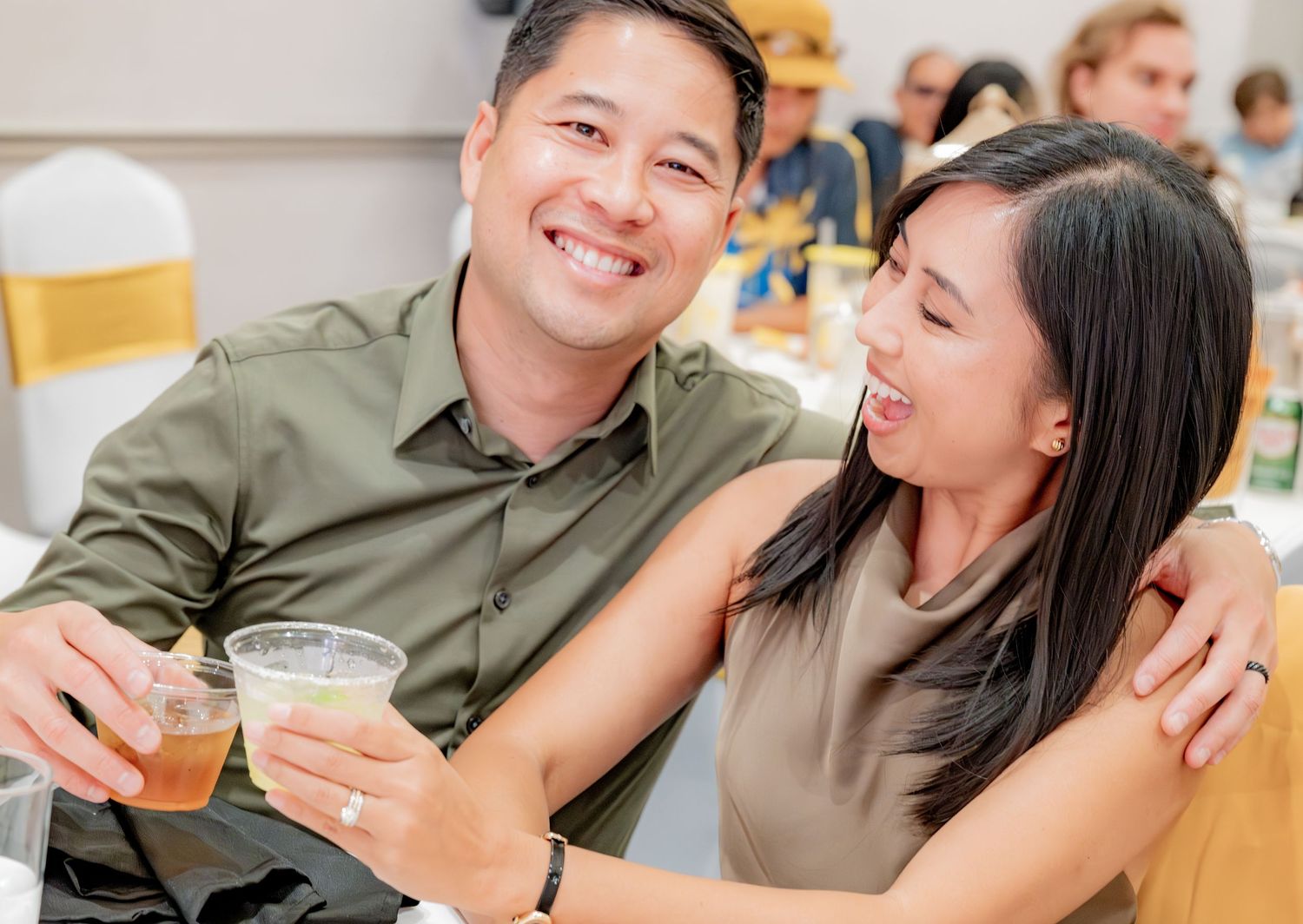 Smiling couple holding drinks and embracing at a festive birthday party celebration dinner.