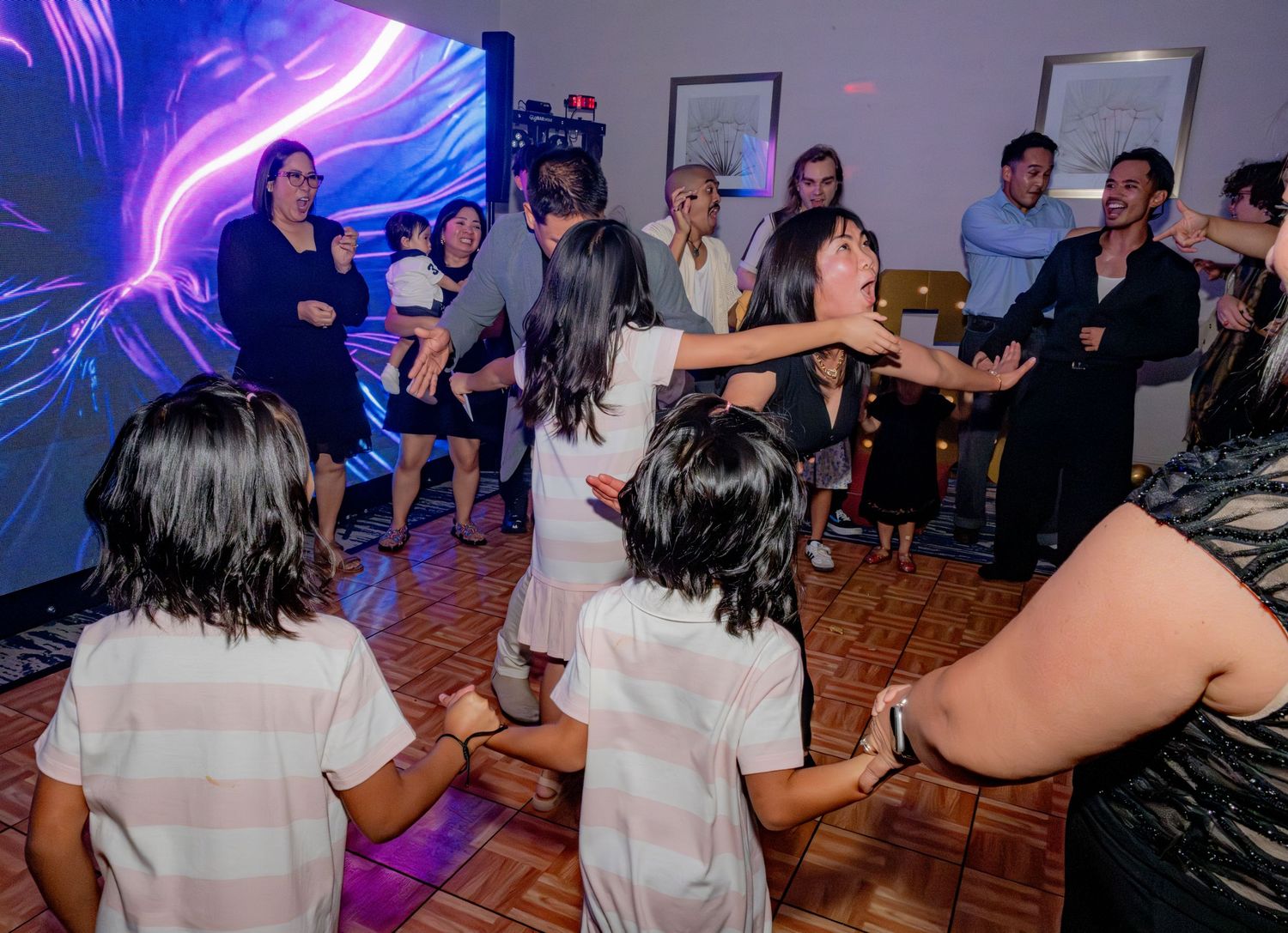 Children and adults dancing energetically on a dance floor at an indoor party event.