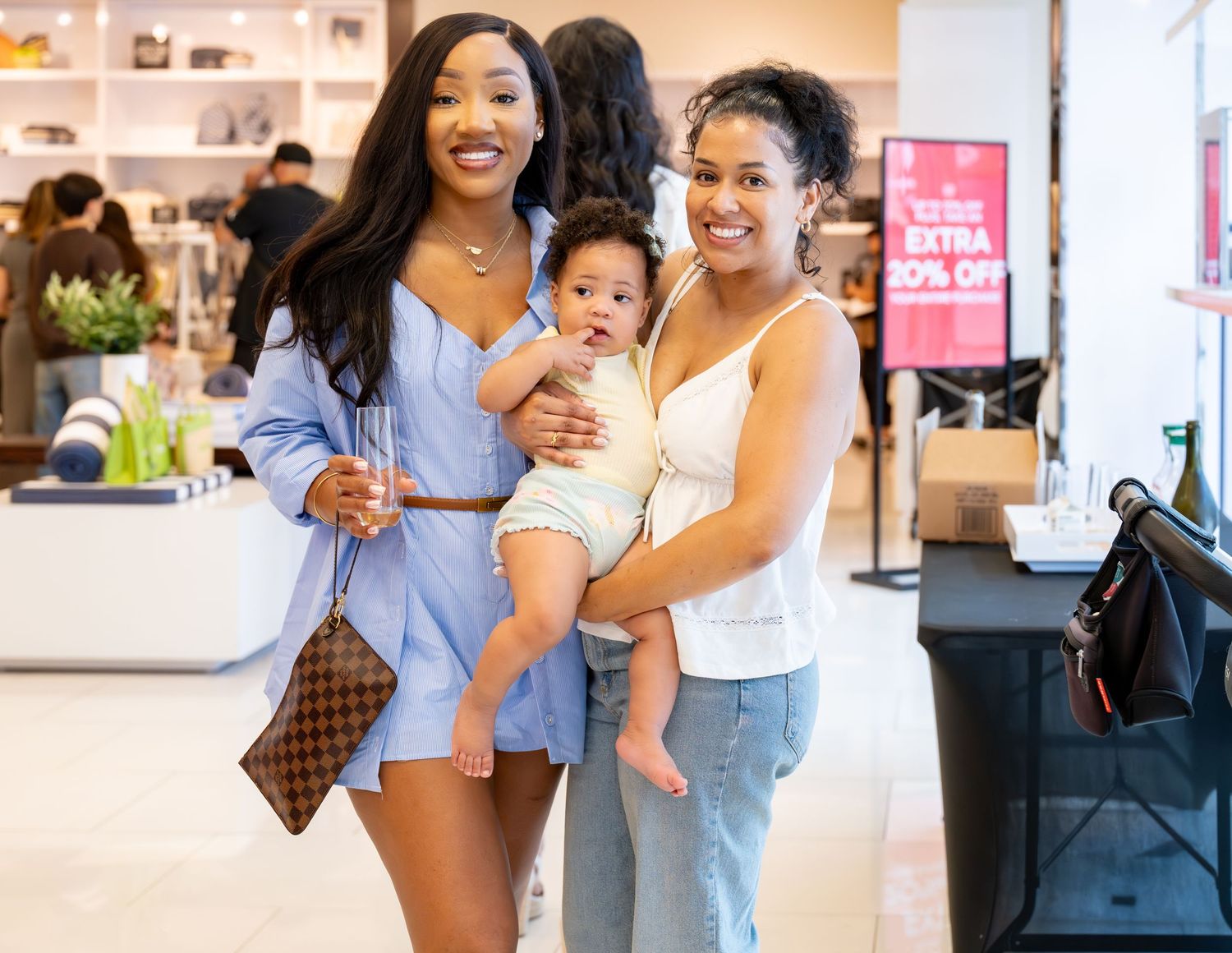 Two women and a baby smiling together inside a busy retail store.
