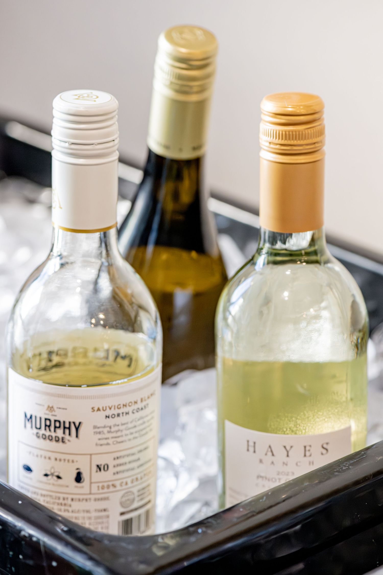 Three white wine bottles including Murphy Goode and Hayes Ranch chilling in an ice bucket.