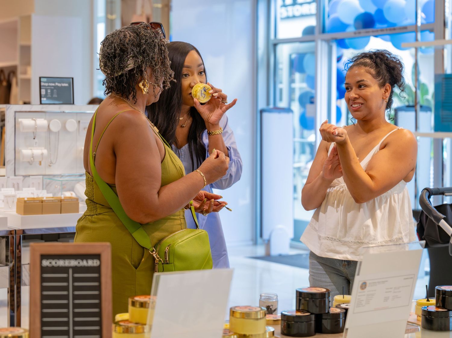 Three women sample beauty products at a retail store display.